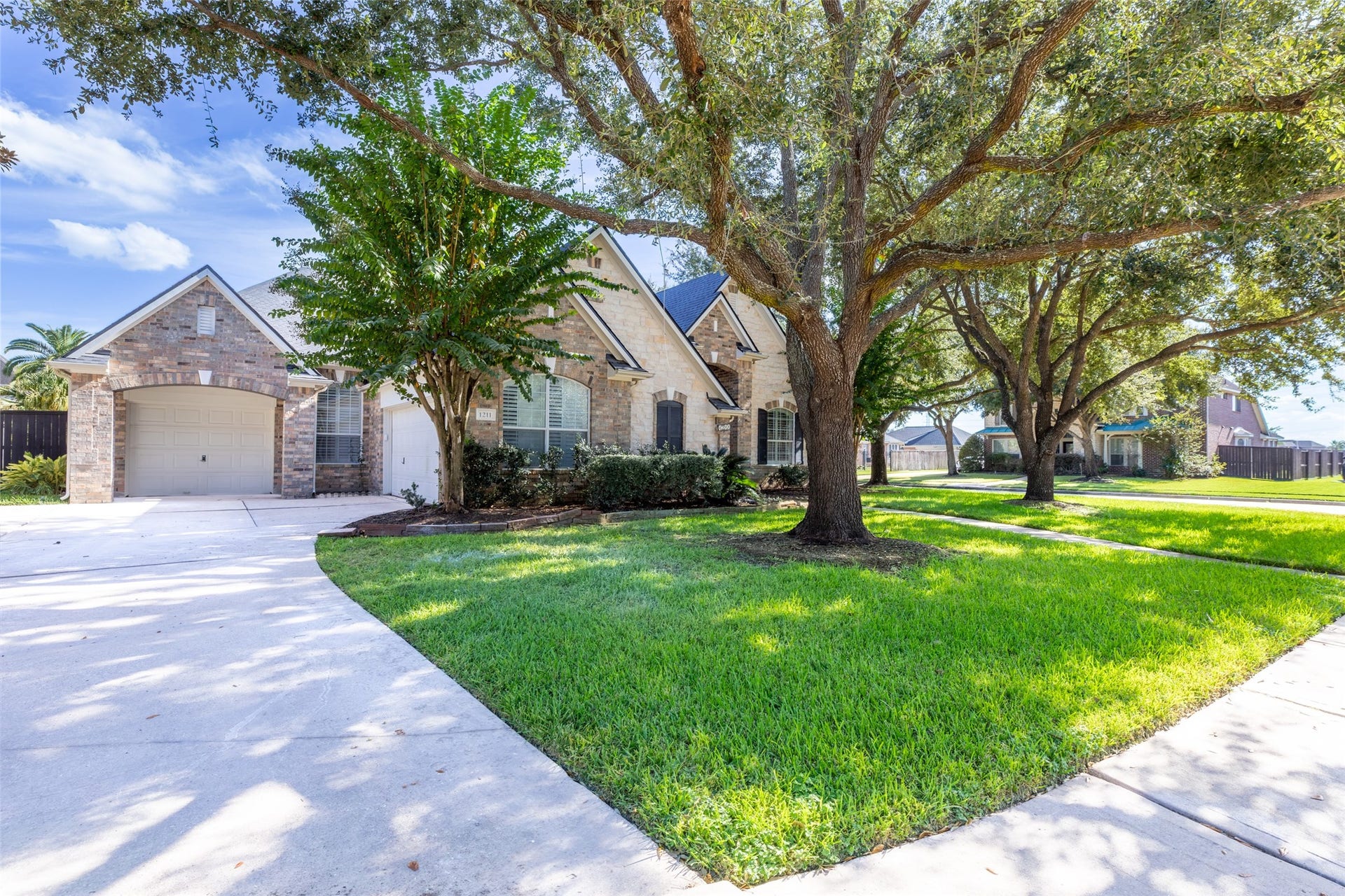 1211 Sterling Court, Katy, TX 77494 Charming stone-accented home with lush landscaping, mature trees, and a spacious driveway leading to a three-car garage.