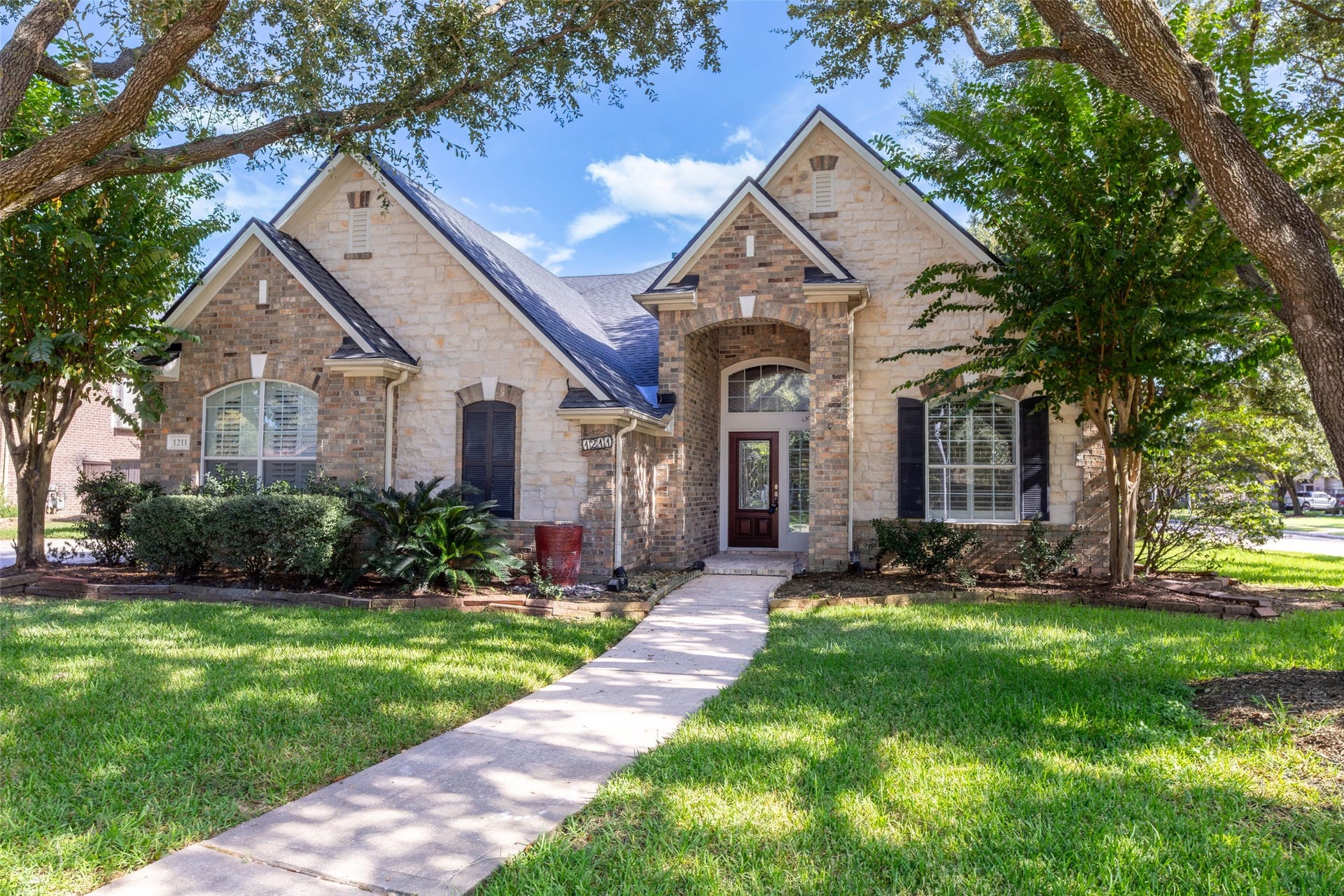 1211 Sterling Court, Katy, TX 77494 Charming stone-front home with a welcoming arched entryway, nestled among mature trees and lush landscaping.