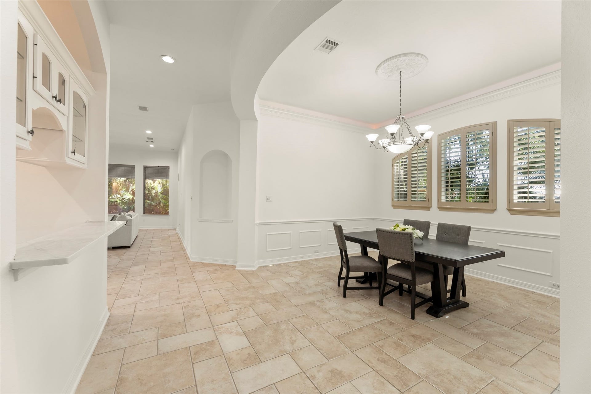 1211 Sterling Court, Katy, TX 77494 Elegant dining area with a stylish chandelier and large windows offering plenty of natural light, complemented by an elegant tiled floor and adjacent open hall with built-in shelves.