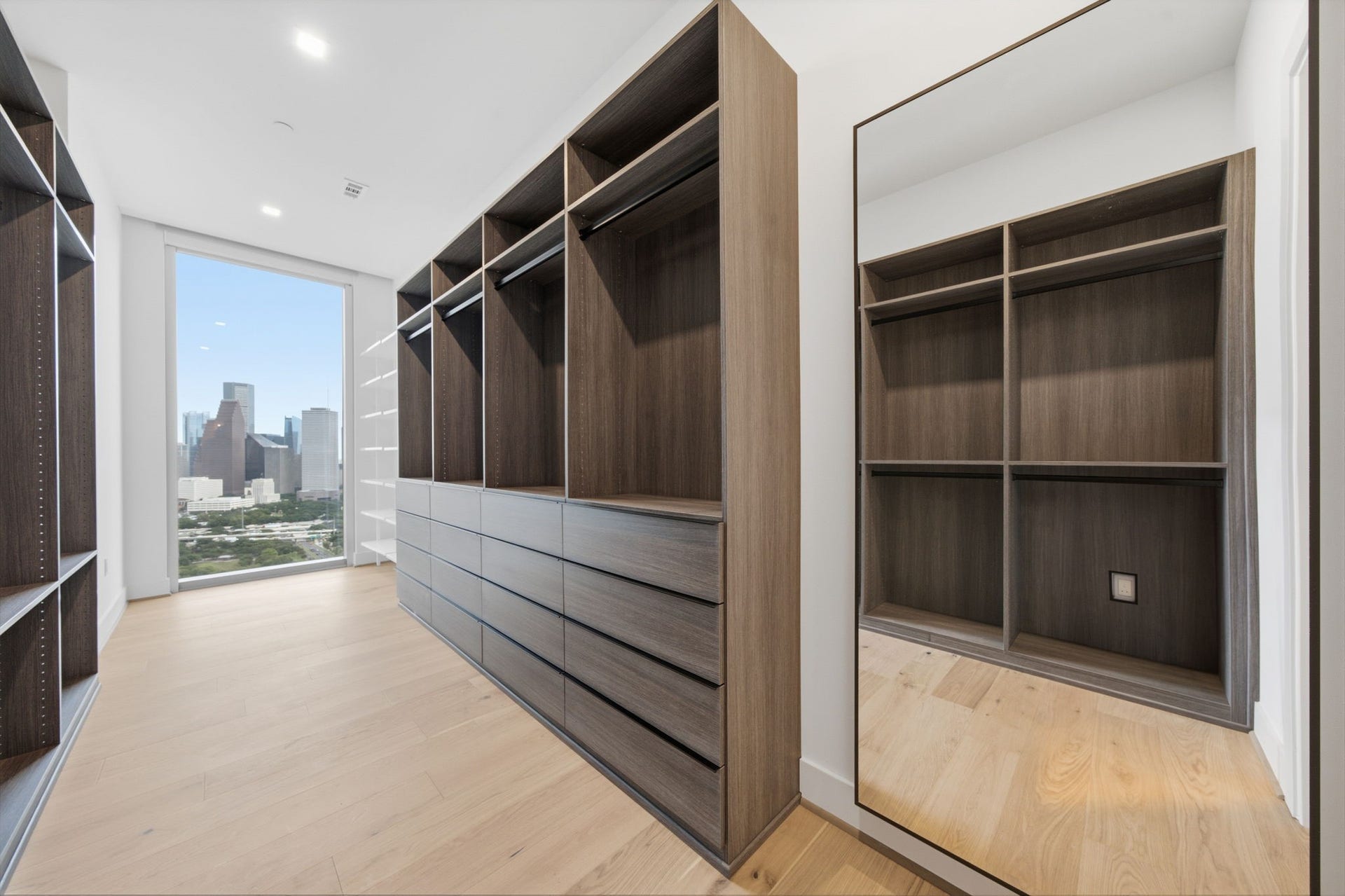 Custom walk in closet designed by California Closets, featuring a floor to ceiling shoe display, and rare Downtown Houston skyline views that bring natural light and luxury into your daily routine.