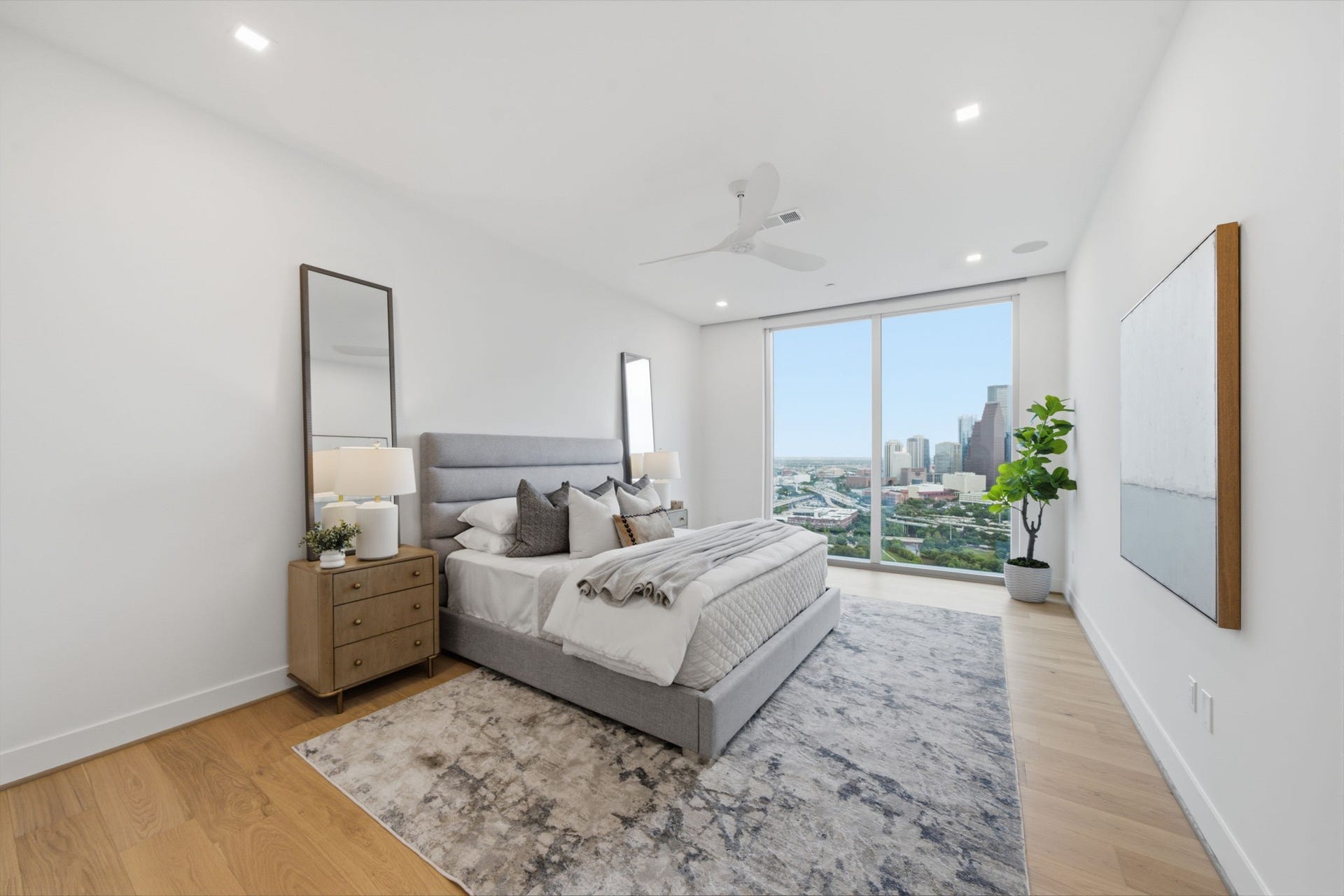 The luxurious primary suite offers a serene escape high above the city, featuring floor to ceiling windows with breathtaking Downtown Houston views, custom motorized blackout shades, and a sophisticated atmosphere designed for rest, privacy, and relaxation.