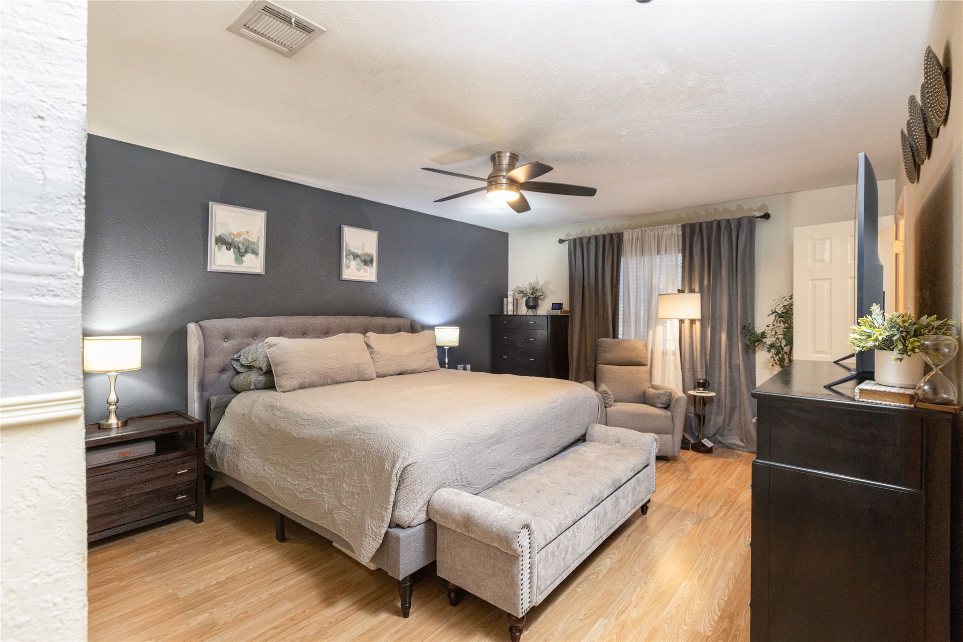 14007 Lorne Drive, Houston, TX 77049 Spacious bedroom featuring a cozy bed, elegant dark accent wall, and modern ceiling fan, complemented by stylish furniture and warm wood flooring.