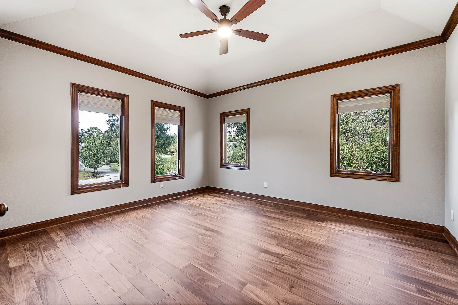 This secondary bedroom features new hardwood floors, crown molding, and multiple windows with treetop views.