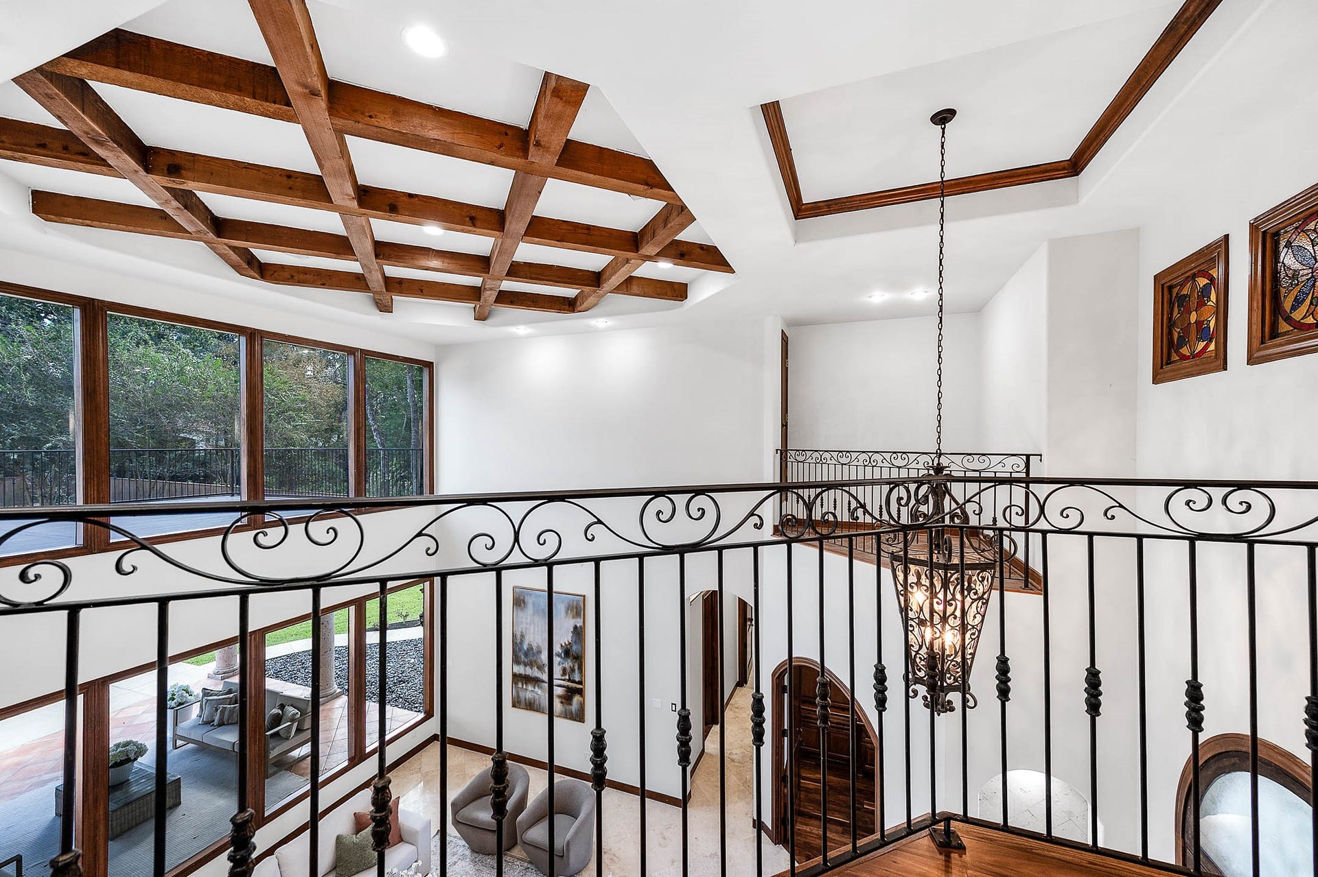 The second-floor landing features exposed wood beams and a wrought iron overlook into the formal living room.