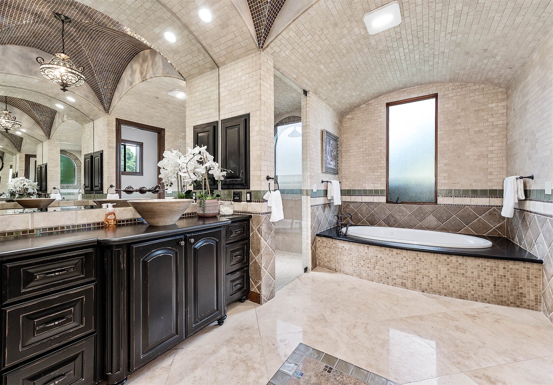 A soaking tub framed in mosaic tile sits separate from the steam shower, beneath a privacy window.