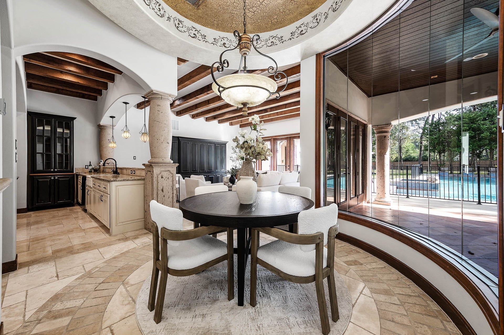 The breakfast room is wrapped in a curved wall of windows overlooking the pool, beneath a decorative domed ceiling.
