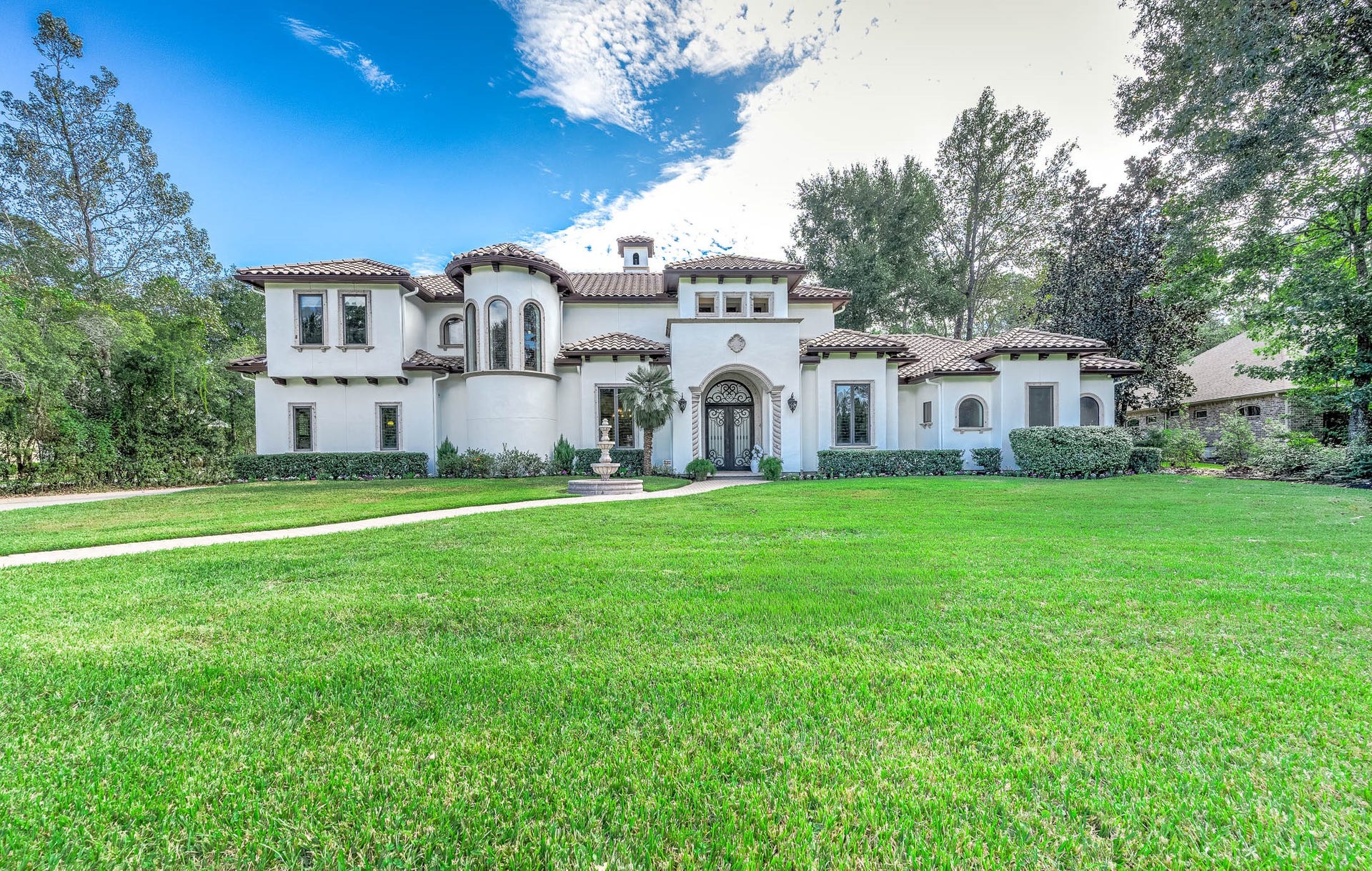 Manicured landscaping and large mature trees frame the home's expansive front lawn and stucco facade.