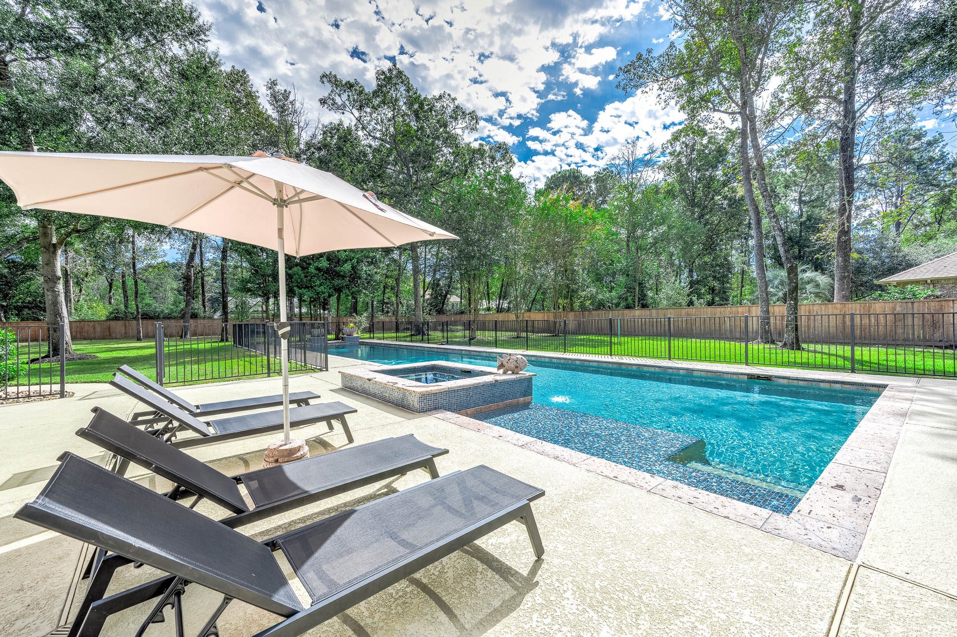 The pool deck offers ample space for lounging beneath large mature trees.