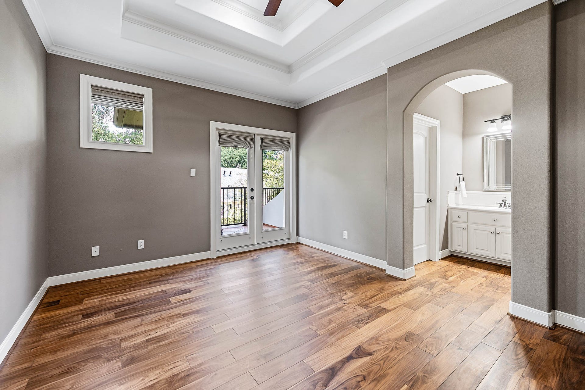 This secondary bedroom features new hardwood floors, a tray ceiling, an ensuite bath, and French doors to a private balcony.