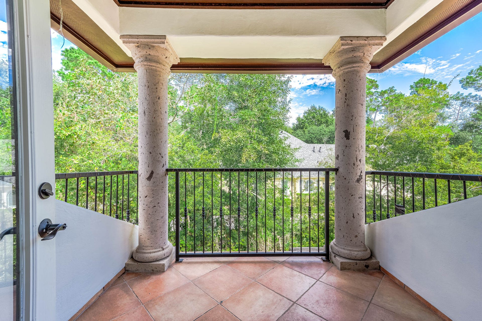 A covered balcony with Cantera stone columns overlooks the mature tree canopy.