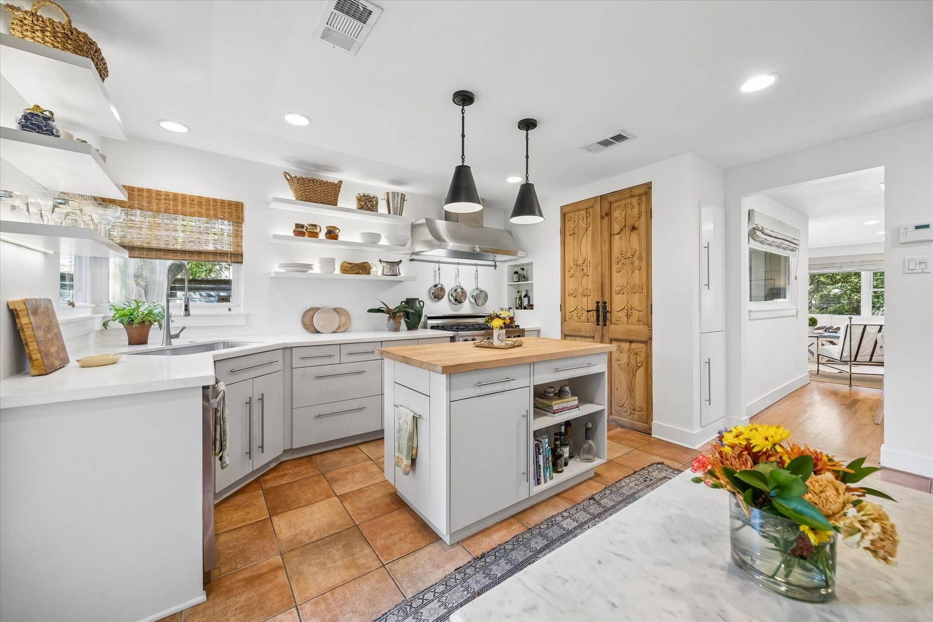 Charming kitchen with open shelving, modern fixtures, and a central island with a butcher block top. The elegant antique wood french doors open to the pantry.