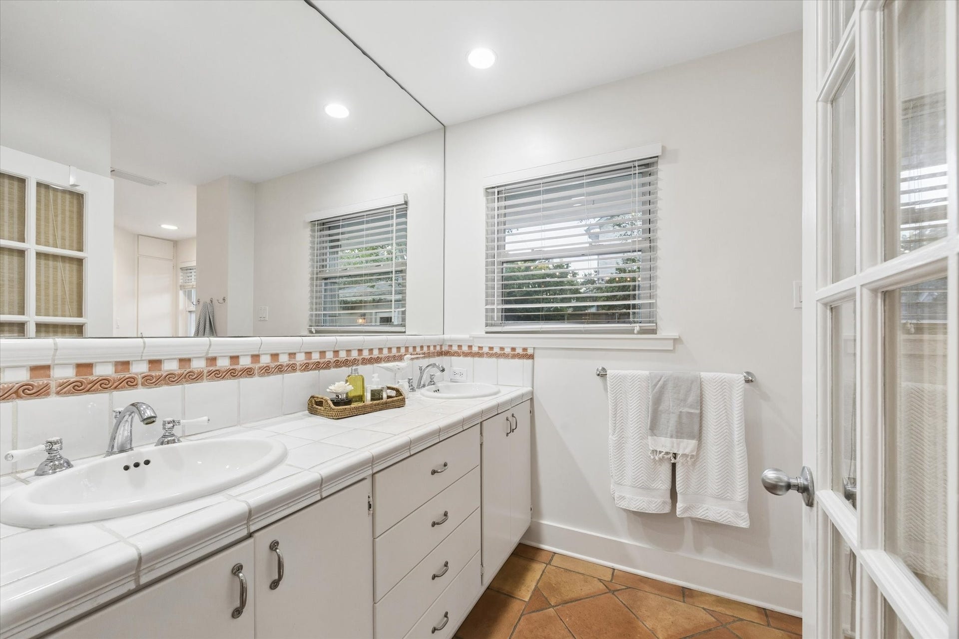 Bright and inviting bathroom featuring a spacious dual-sink vanity, elegant tile countertops, and large mirrors that enhance the sense of space.