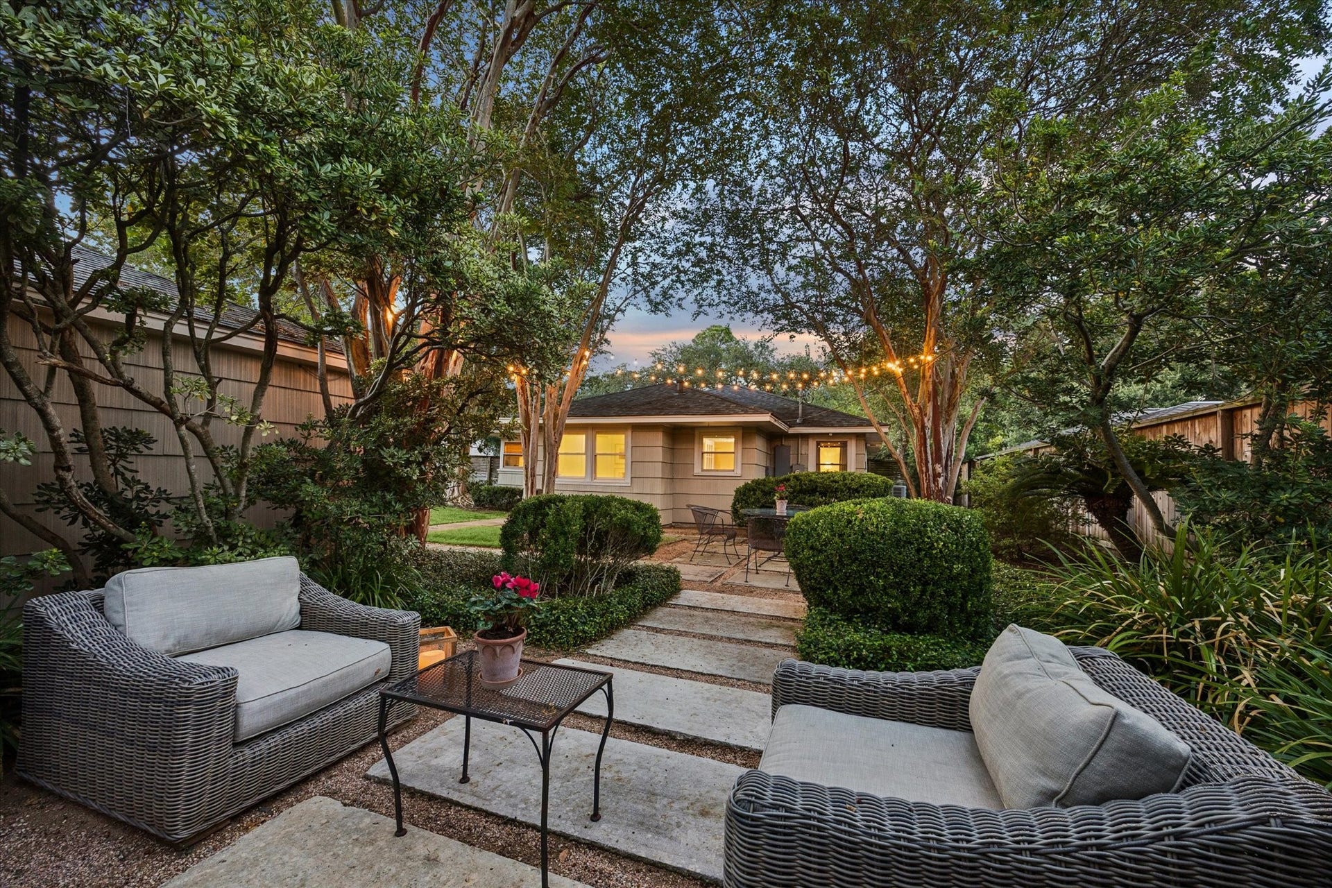 Charming backyard oasis with cozy seating, lush greenery, and ambient string lighting, perfect for relaxing and entertaining.