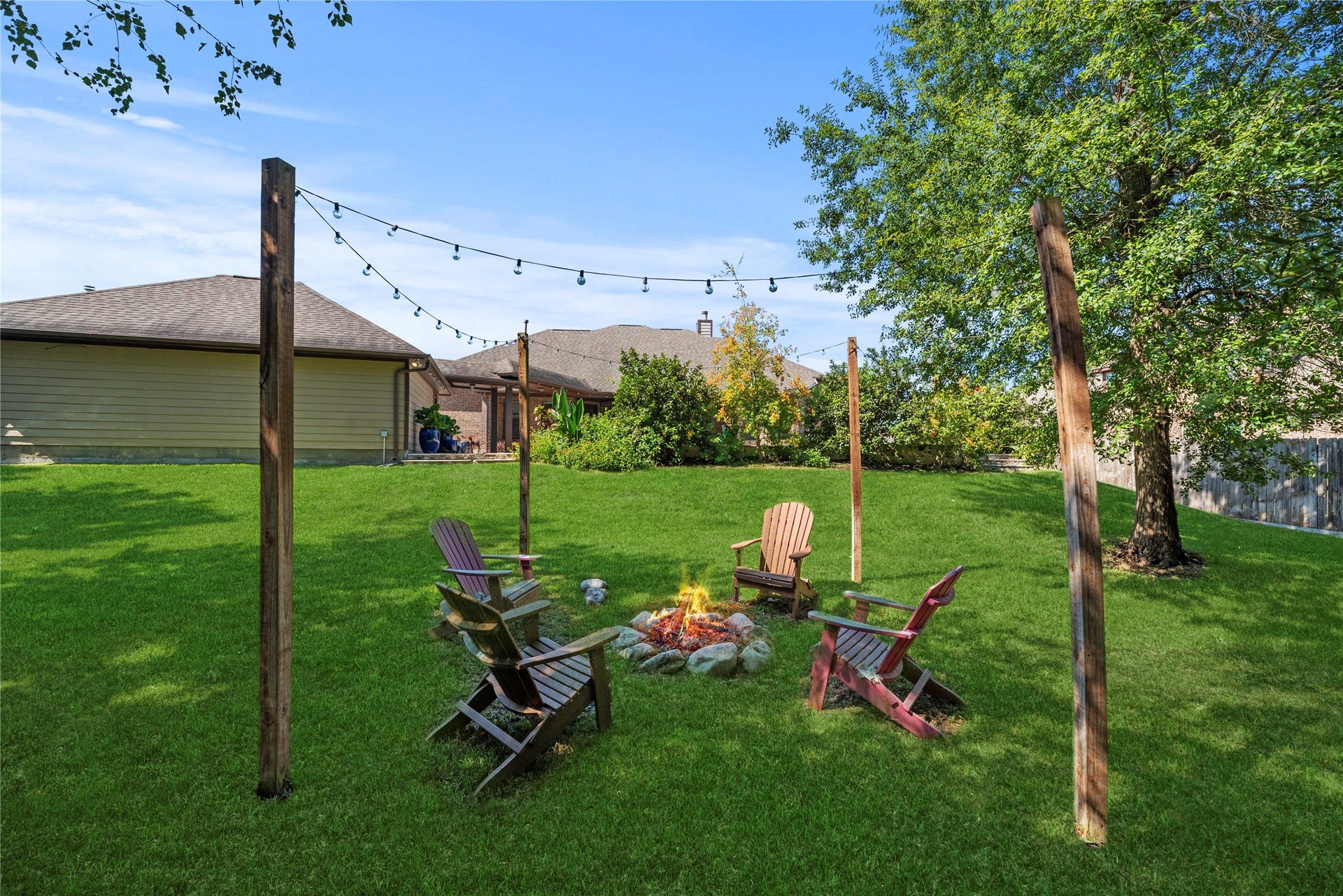 12522 Savage Court, Magnolia, TX 77354 The perfect gathering spot featuring a charming fire pit surrounded by overhead string lighting, a lush green lawn, and mature shade trees.