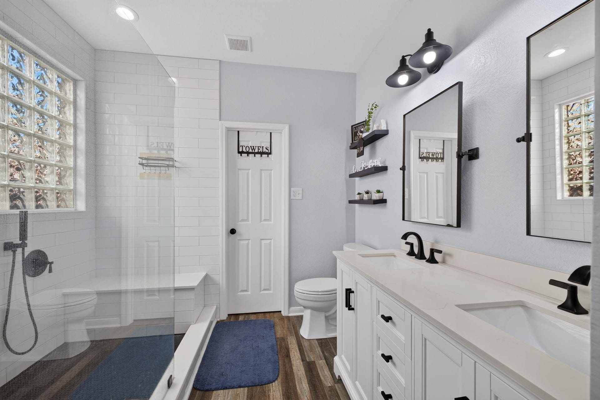 17307 Thicket Hollow Lane, Cypress, TX 77429 Modern bathroom with a sleek double vanity and black fixtures. Features a spacious glass-enclosed shower, subway tile, and natural light from glass block windows.