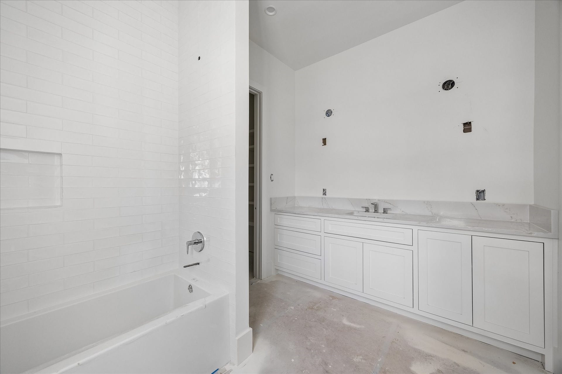 915 Lamonte Lane, Houston, TX 77018 Wide vanity cabinetry extends the counter around a single basin, combining drawer storage with enclosed cabinets beside the tub. White tile continues up the bathing wall and around a recessed niche. Mirror, lighting and final trim remain in progress.