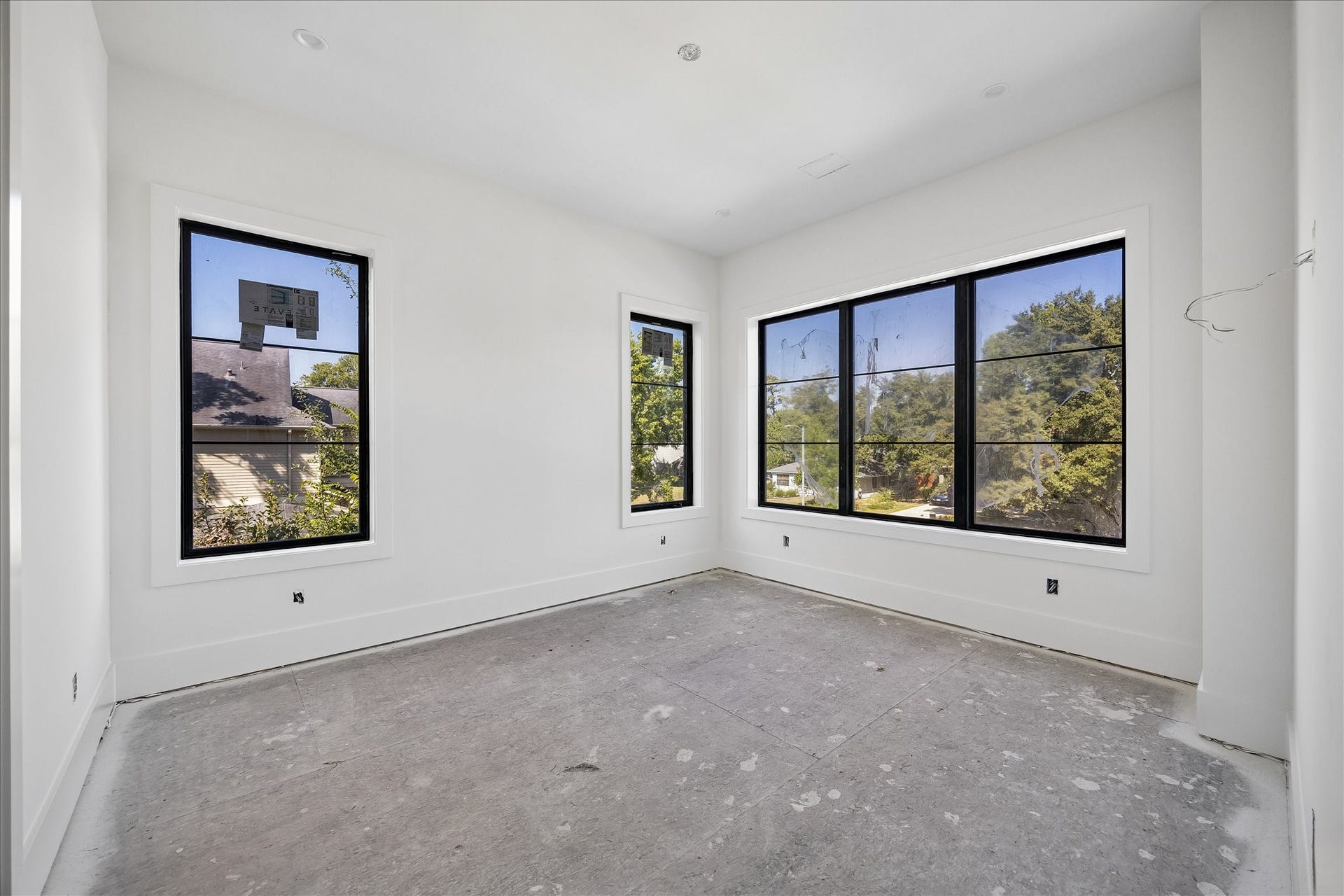 915 Lamonte Lane, Houston, TX 77018 Windows on 2 walls bring daylight from different directions, including a broad view toward the trees outside. Black frames contrast with the light wall and trim palette, while the uninterrupted wall areas leave room for the space's intended use. Final flooring is still underway.