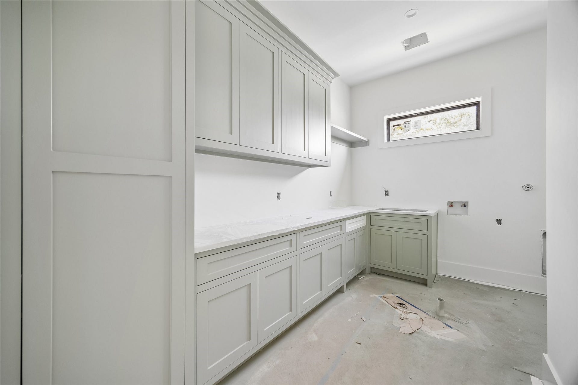 915 Lamonte Lane, Houston, TX 77018 Laundry counters and cabinetry return around the corner, with a sink beneath the horizontal window and a drying rod below the short shelf. Upper cabinets add storage. The builder also confirmed an outlet inside the vacuum storage cabinet for concealed charging; appliances are not installed.