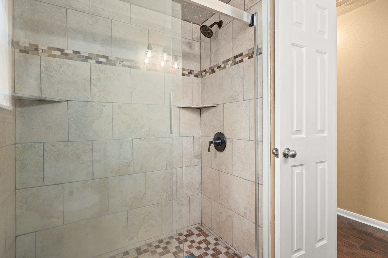 3802 Oakwilde Circle, La Porte, TX 77571 Beautifully Tiled Oversized Shower with Decorative Accents, Glass Enclosure, and Built-In Corner Shelves.