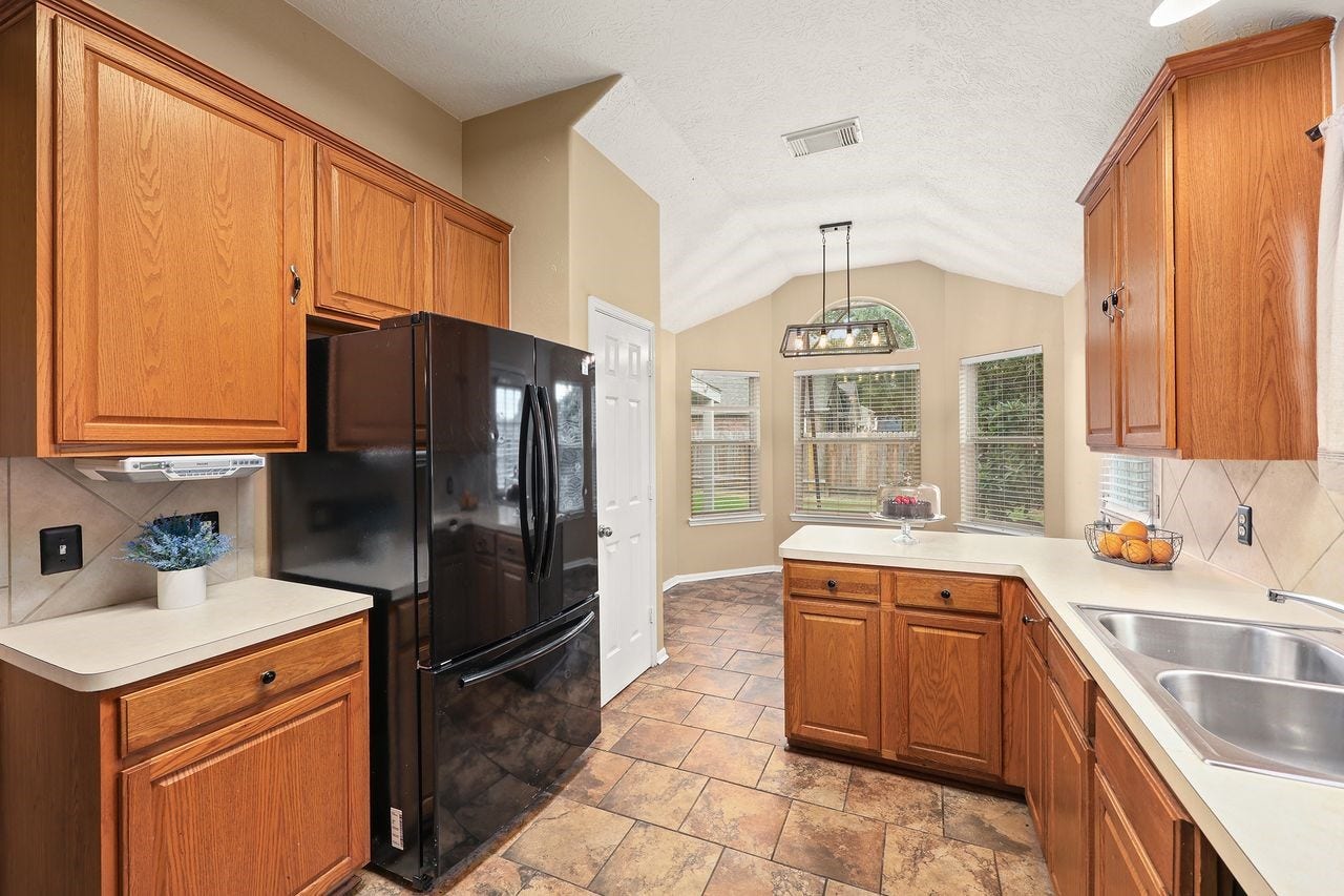 3802 Oakwilde Circle, La Porte, TX 77571 Another View of the Kitchen Showcasing the Refrigerator, Generous Storage, and Bright Breakfast Nook with High Ceiling.