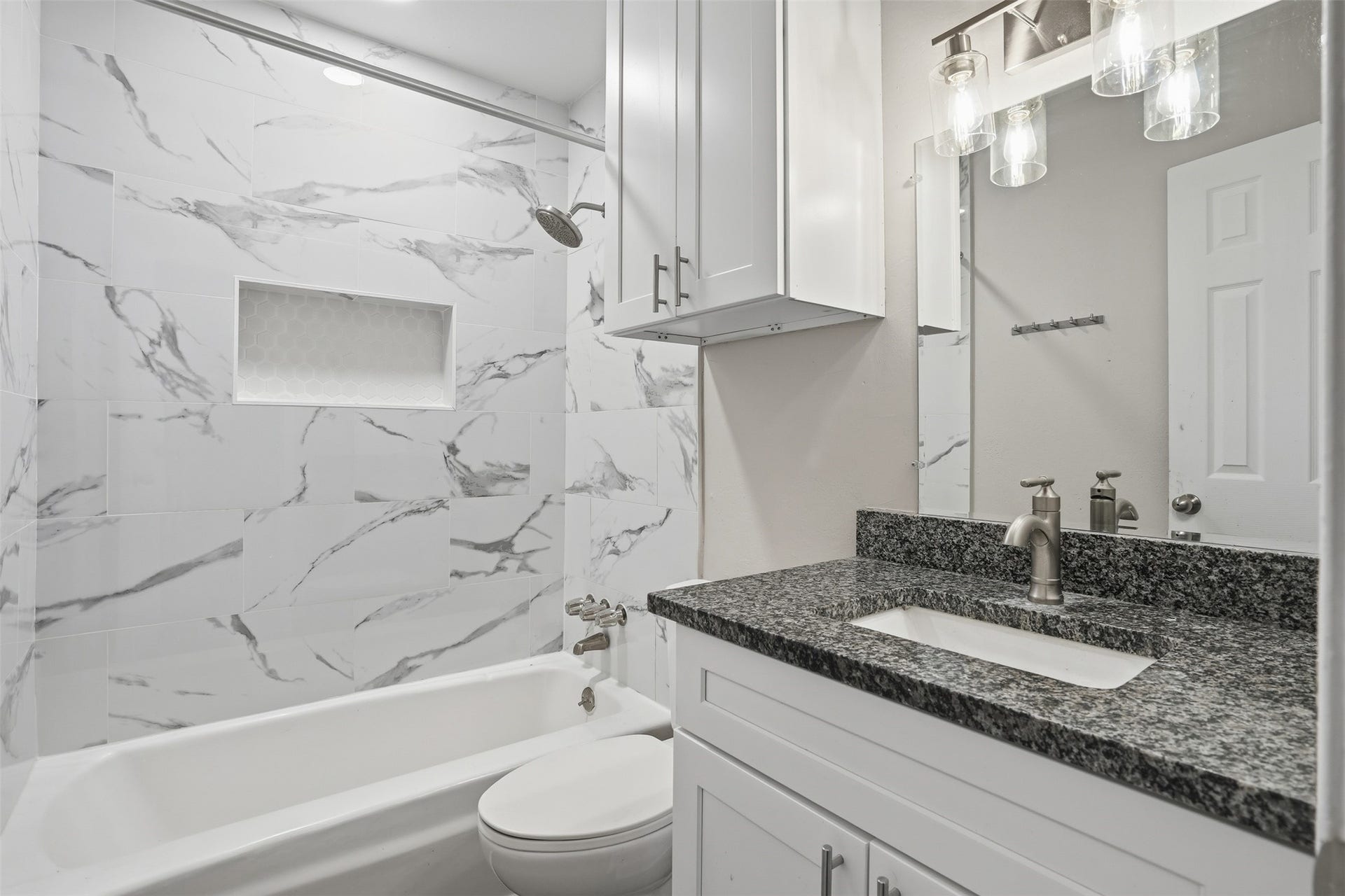 Bright and modern bathroom featuring a tub/shower combination with elegant marble-style tile and a granite countertop vanity.