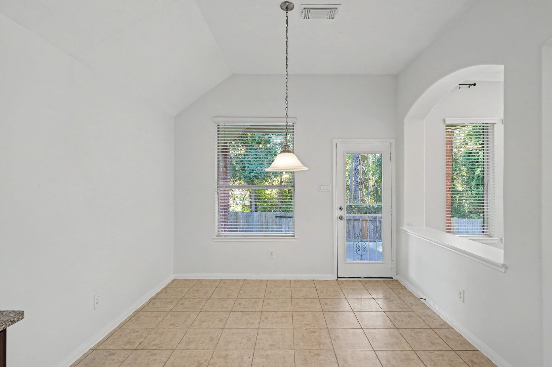 Bright breakfast area featuring vaulted ceilings, tile flooring, pendant lighting and backyard views with convenient outdoor access.