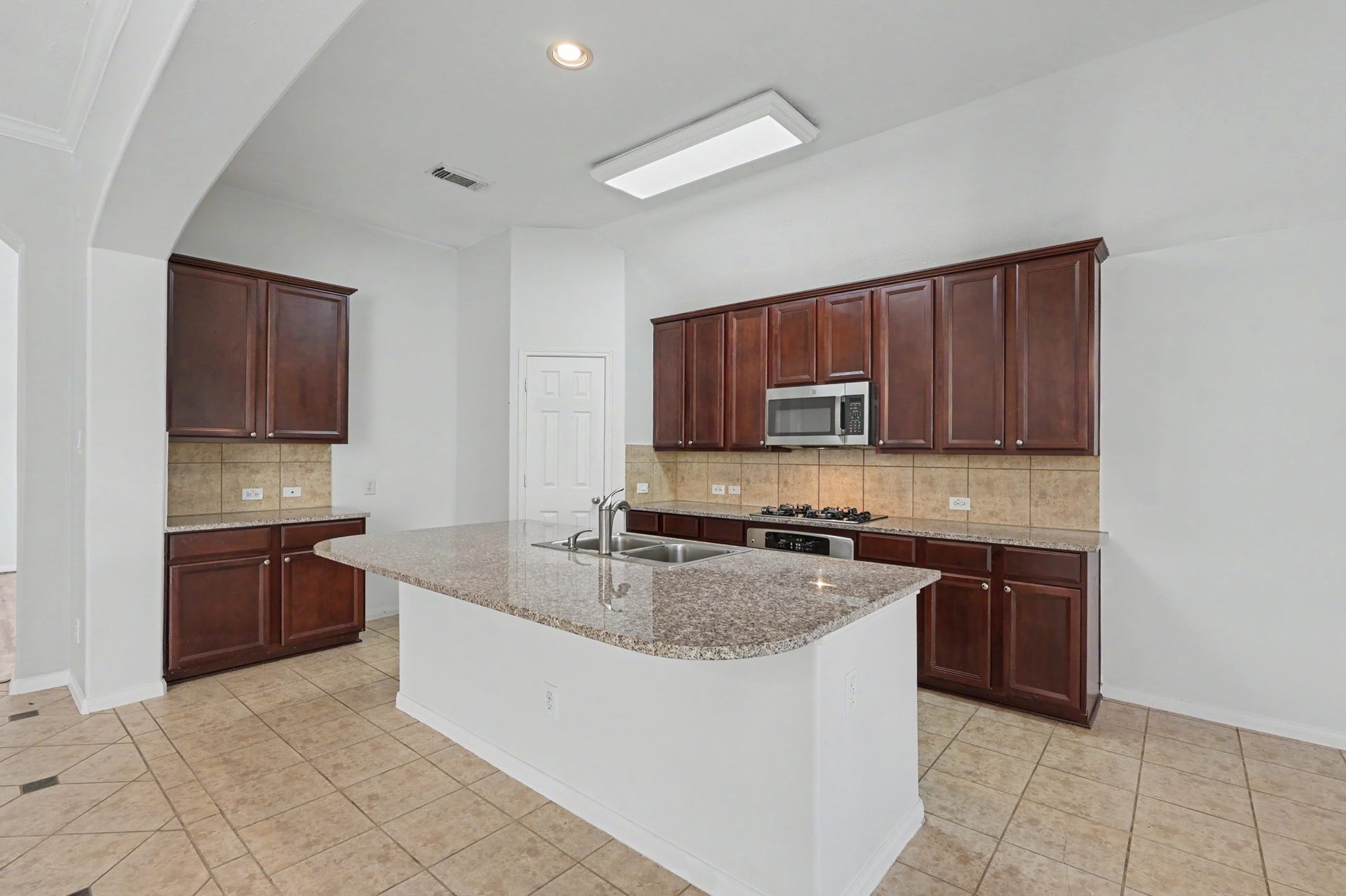 Spacious island kitchen featuring granite countertops, 42" cabinetry, stainless steel appliances, gas cooktop, tile backsplash and corner pantry.