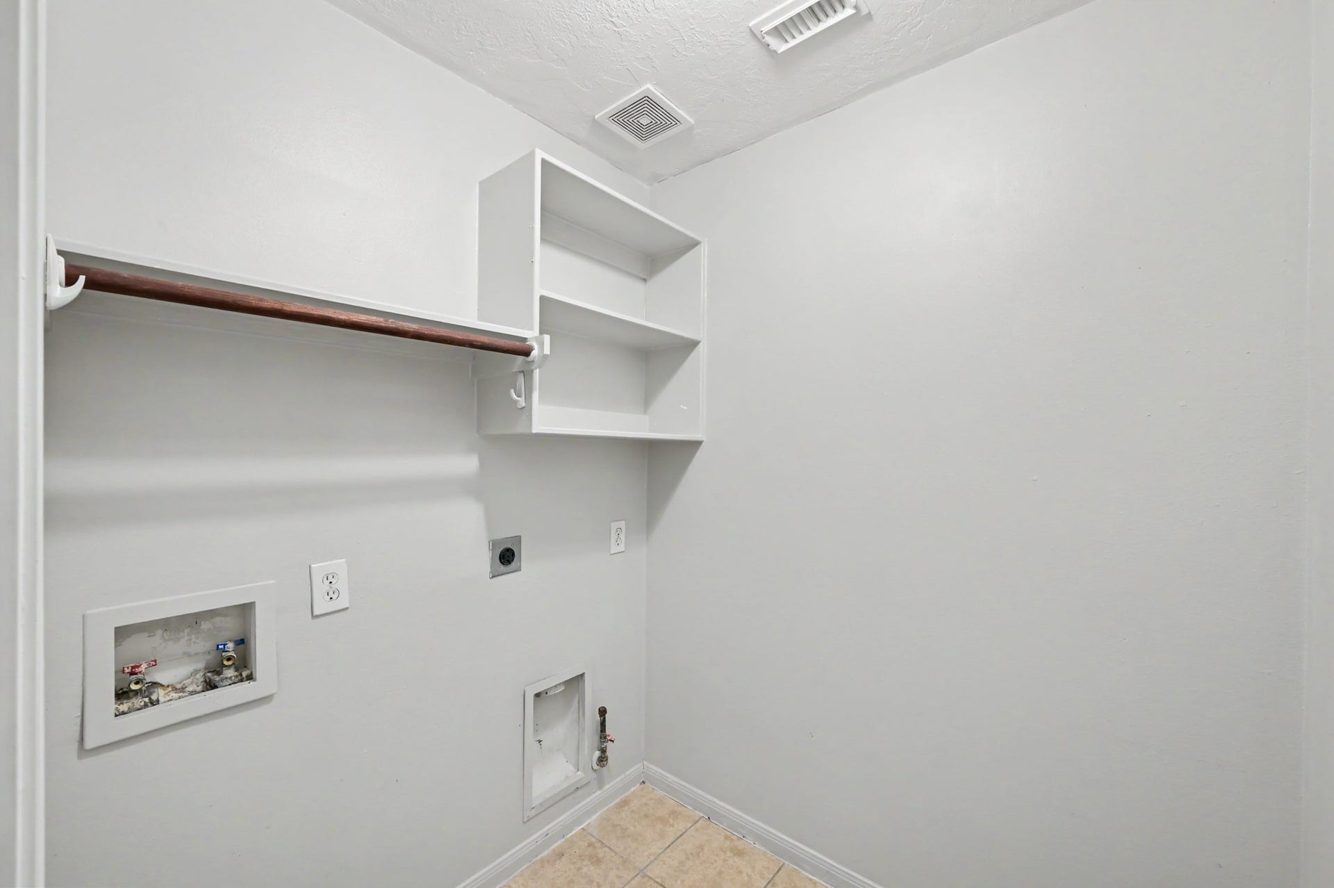 Convenient utility room with washer and dryer connections, built-in shelving and hanging rod for additional storage.