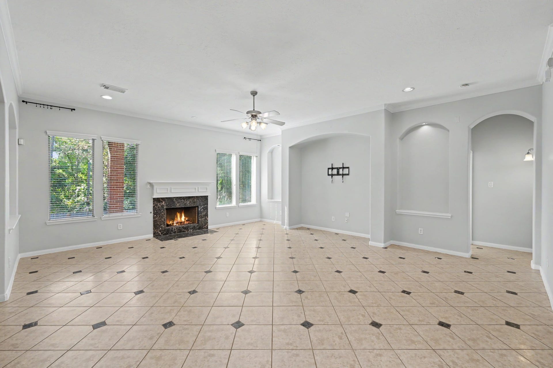 Spacious family room featuring decorative tile flooring, crown molding, cozy fireplace, abundant natural light and an open-concept layout perfect for entertaining.