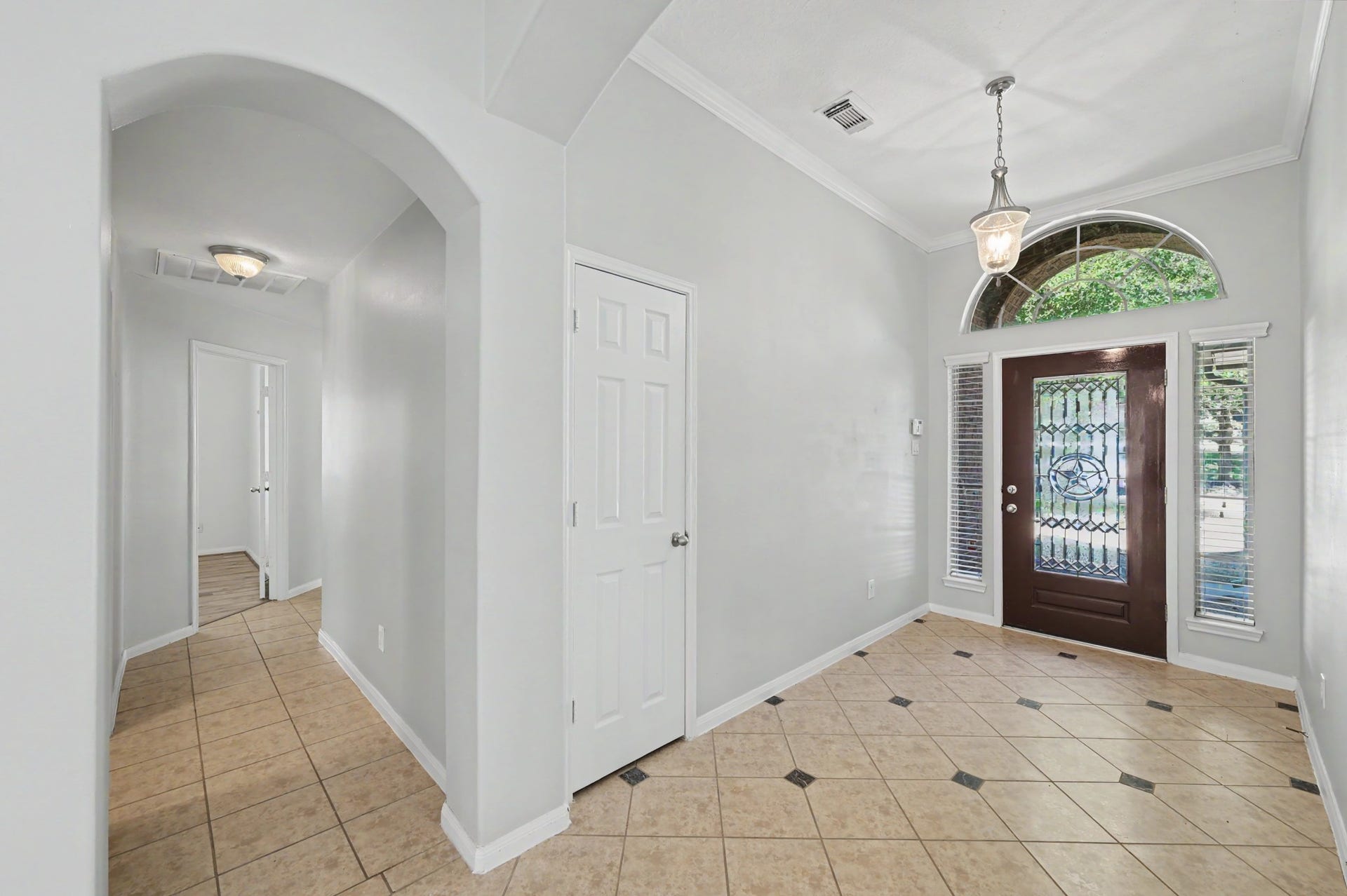 Spacious foyer featuring decorative tile flooring, crown molding, pendant lighting and a beautiful glass front door with arched transom window.