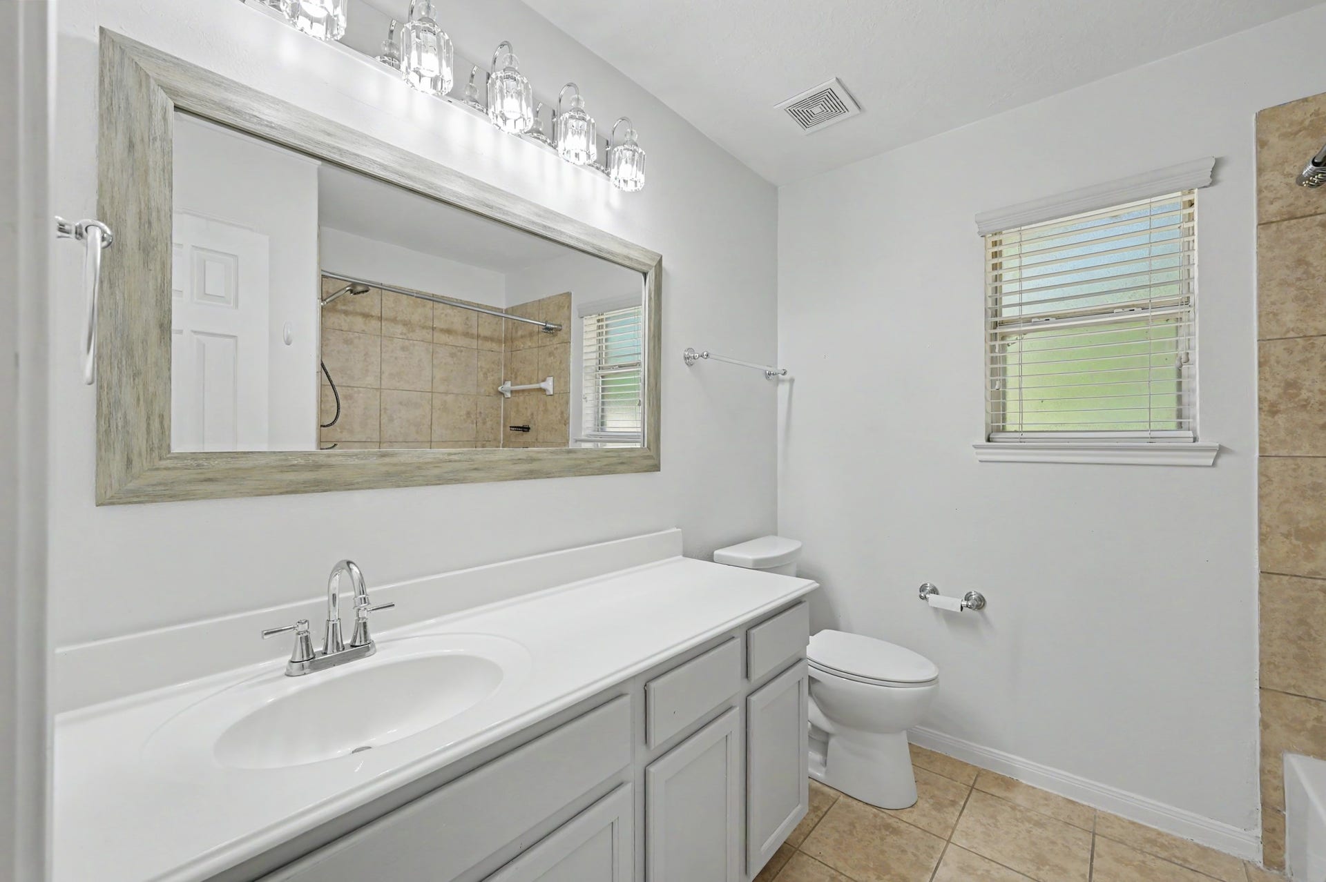 Secondary bath featuring spacious vanity with ample storage, decorative framed mirror, updated lighting and tiled tub/shower combination.