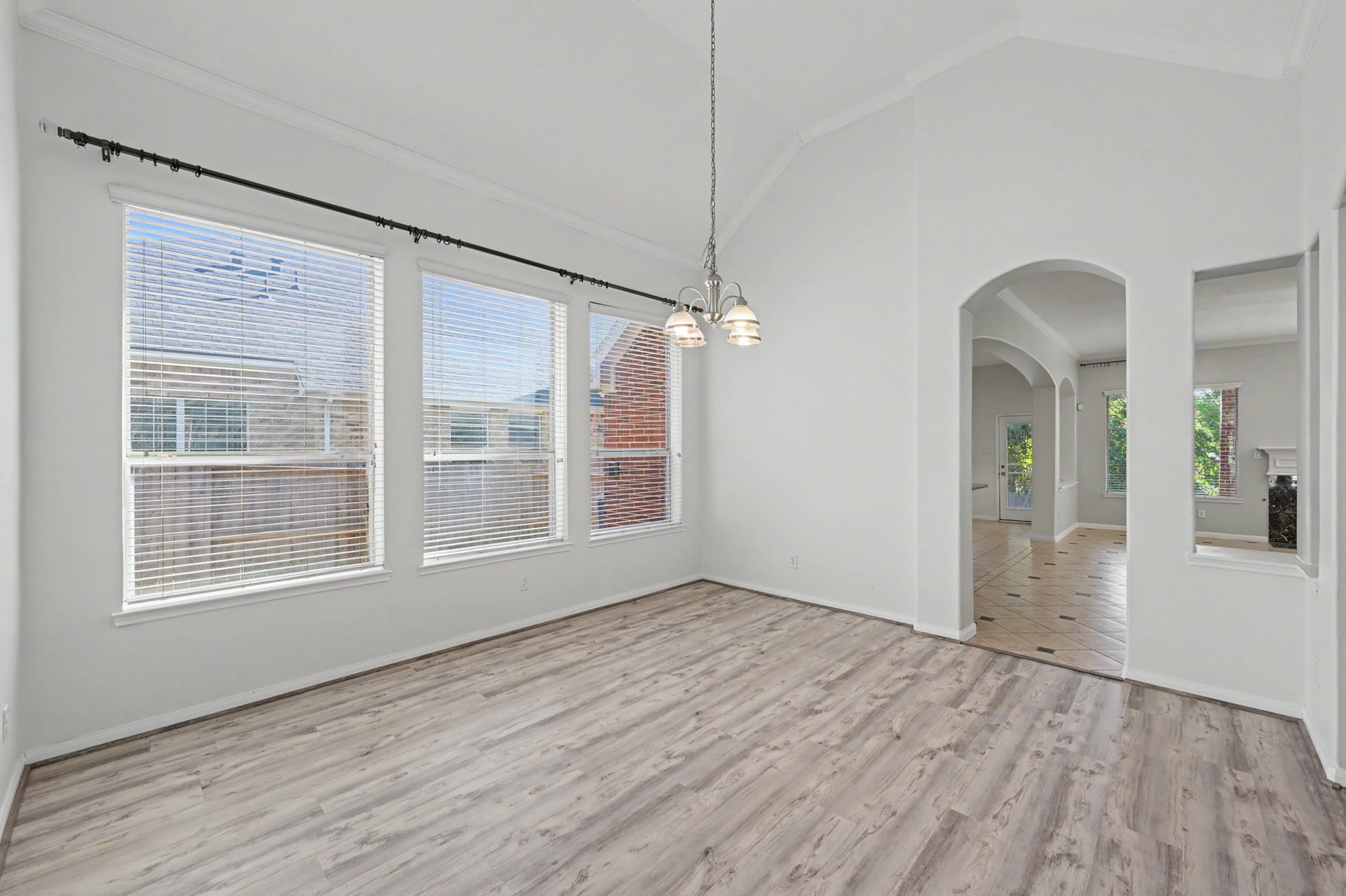 Spacious formal dining room featuring vaulted ceilings, crown molding, wood-look flooring, elegant chandelier and abundant natural light.