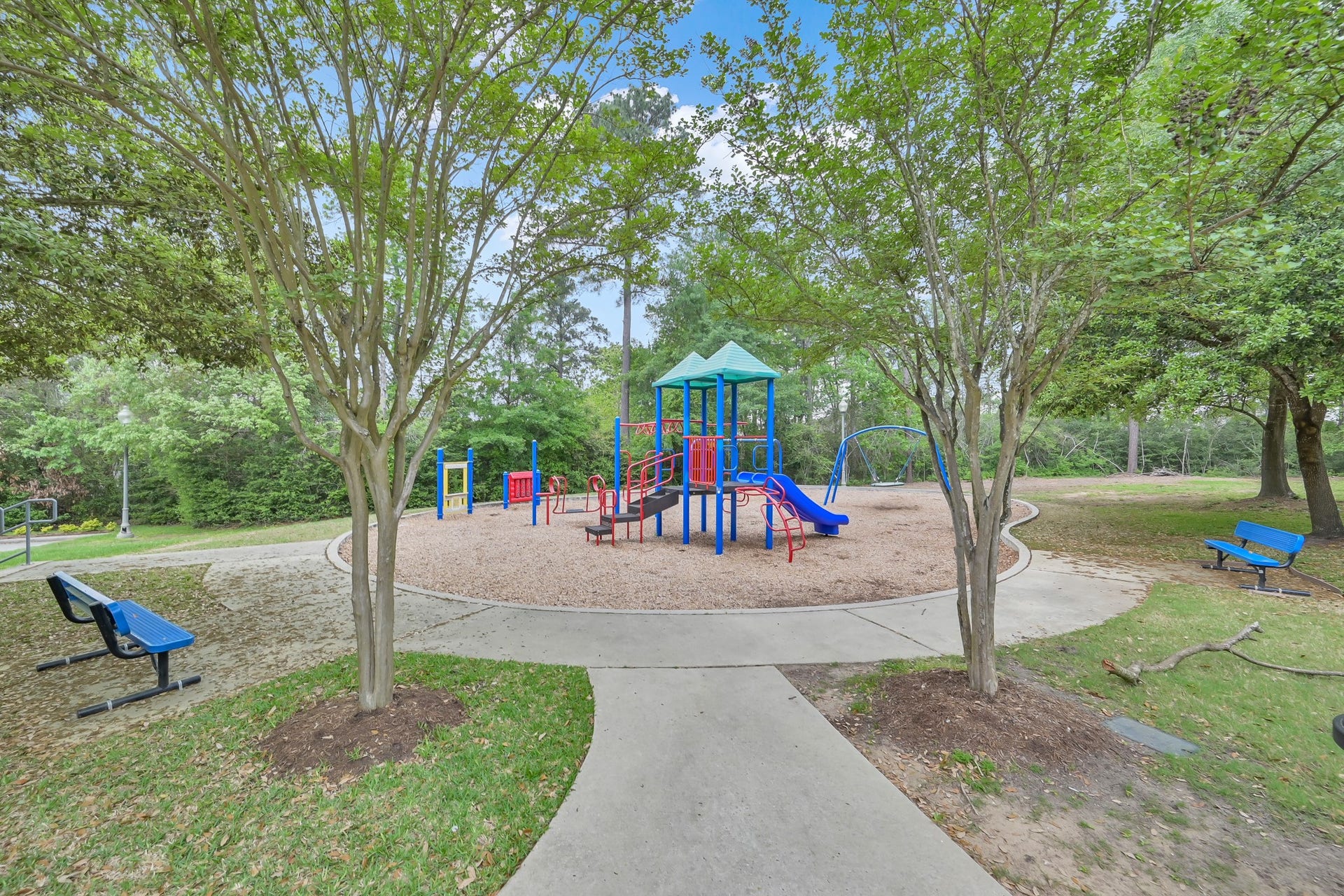 Graystone Hills community playground featuring colorful play equipment, swings, shaded benches and mature trees, providing a fun outdoor space for residents to enjoy!