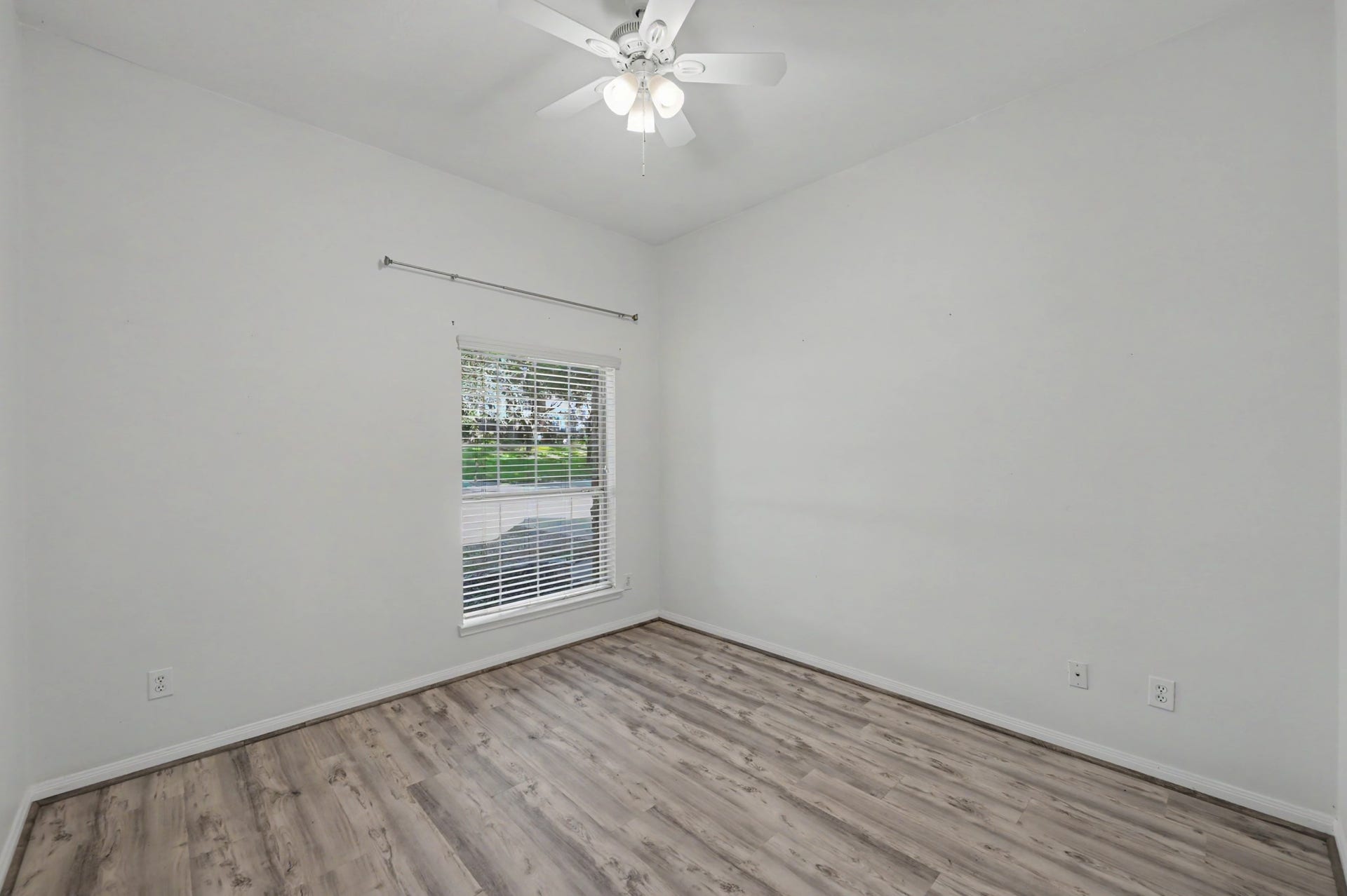 Bright secondary bedroom featuring wood-look flooring, ceiling fan and natural light, perfect for guests or a home office.