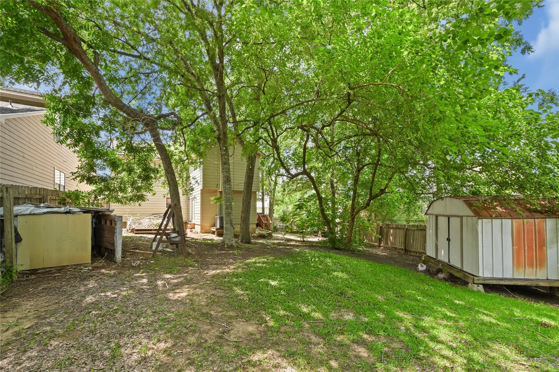 107 Harbour Town Lane, Conroe, TX 77356 A view of the lawn and shaded backyard area, showcasing multiple trees, a perimeter fence, and a partial view of a shed.
