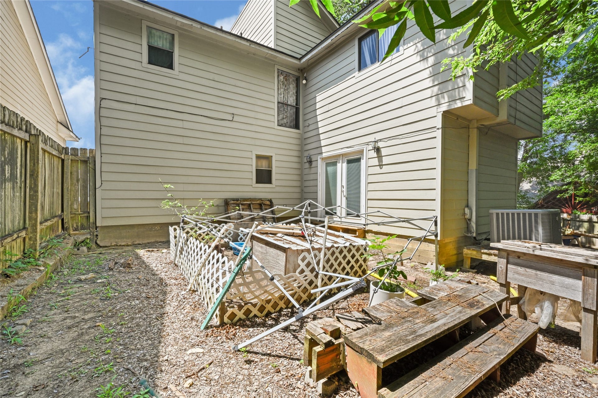 107 Harbour Town Lane, Conroe, TX 77356 A backyard view showcasing the rear exterior of the two-story beige home, featuring a concrete patio area alongside an older wooden picnic table and bench.