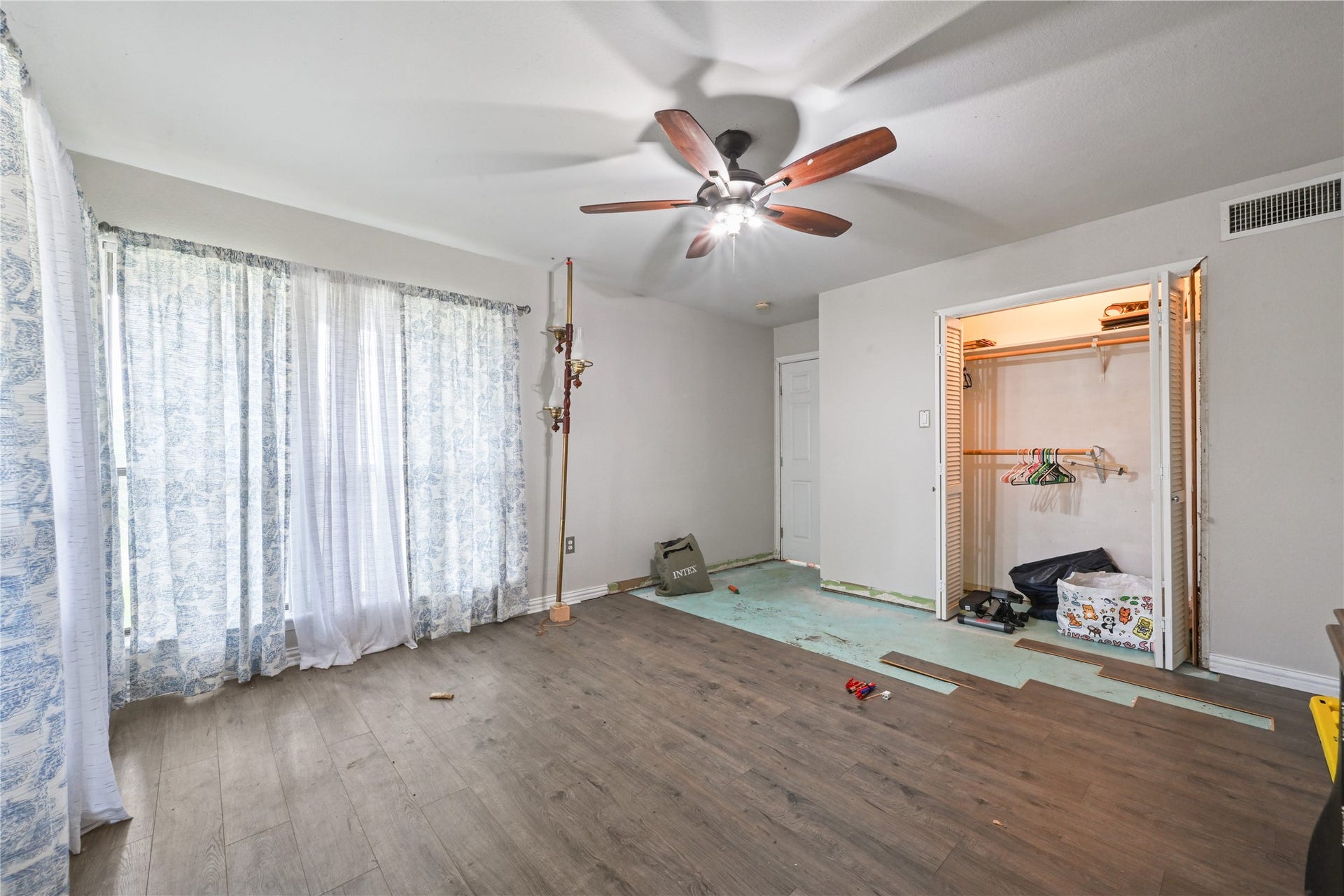 107 Harbour Town Lane, Conroe, TX 77356 A bright, expansive bedroom showcasing a large window wall with privacy curtains, a ceiling fan, and a spacious double closet.