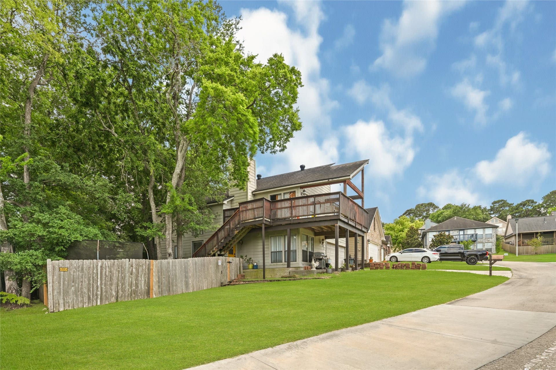107 Harbour Town Lane, Conroe, TX 77356 Wide-angle view from the street showcasing the home's prominent elevation, driveway layout, and surrounding neighborhood tree canopy.