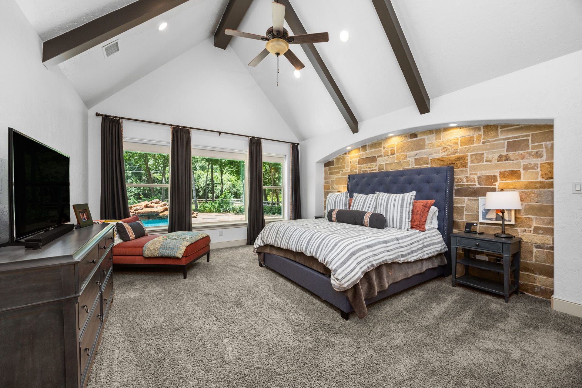 2734 Forest View, Richmond, TX 77406 Primary downstairs bedroom with ensuite bath. Inset stone wall at headboard area. A striking wood beam ceiling and a splendid pool and backyard view.
