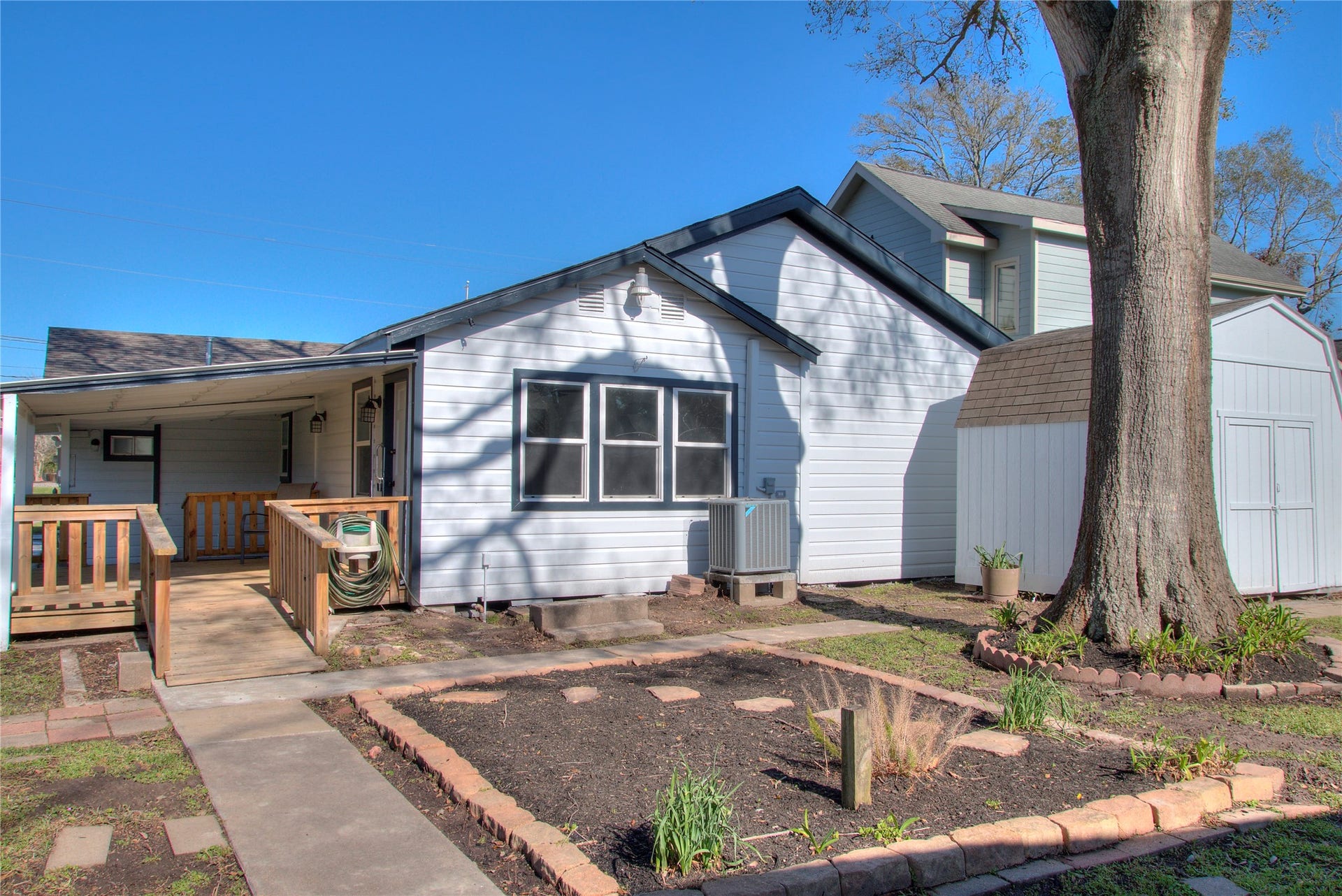 415 Perkins Avenue, League City, TX 77573 Charming covered patio with a wooden deck, convenient ramps, and a mature shade tree overlooking a cozy garden area.