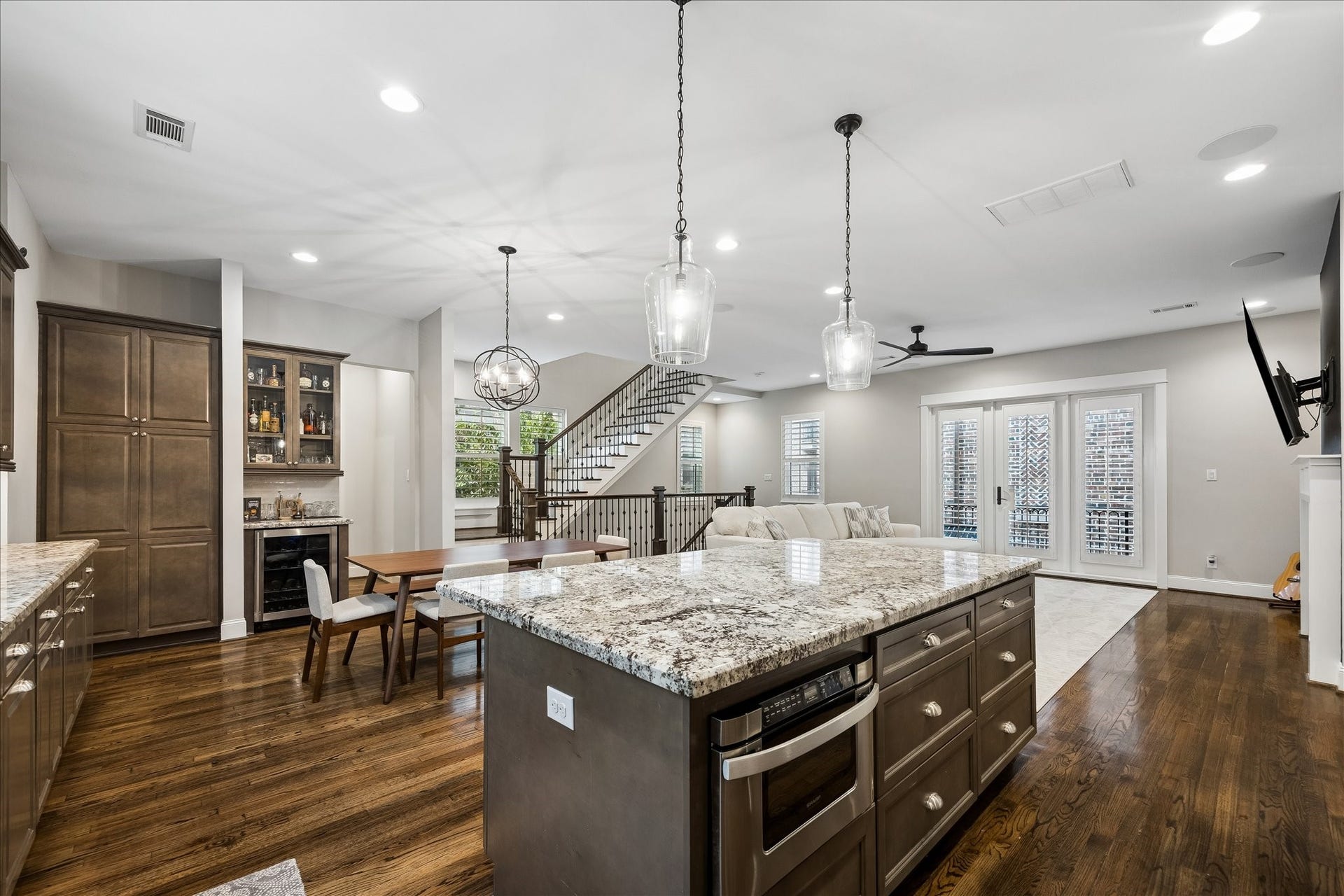 2915 Hicks Street, Houston, TX 77007 Spacious open-concept living area featuring a stunning kitchen island with granite countertops, elegant pendant lighting, and warm hardwood floors. The area seamlessly flows into a cozy living space with large windows and French doors leading outside.