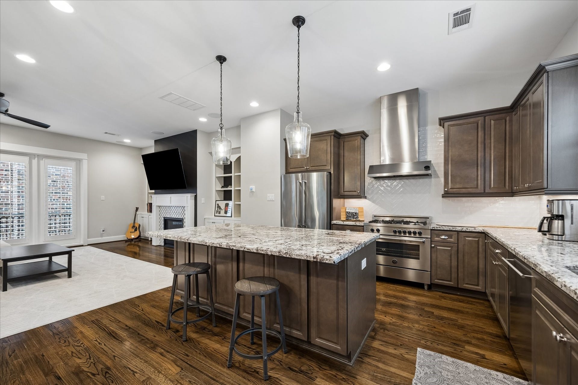 2915 Hicks Street, Houston, TX 77007 Spacious kitchen with elegant granite countertops, stainless steel appliances, and rich wood cabinetry, seamlessly flowing into a cozy living area with a fireplace and large windows.