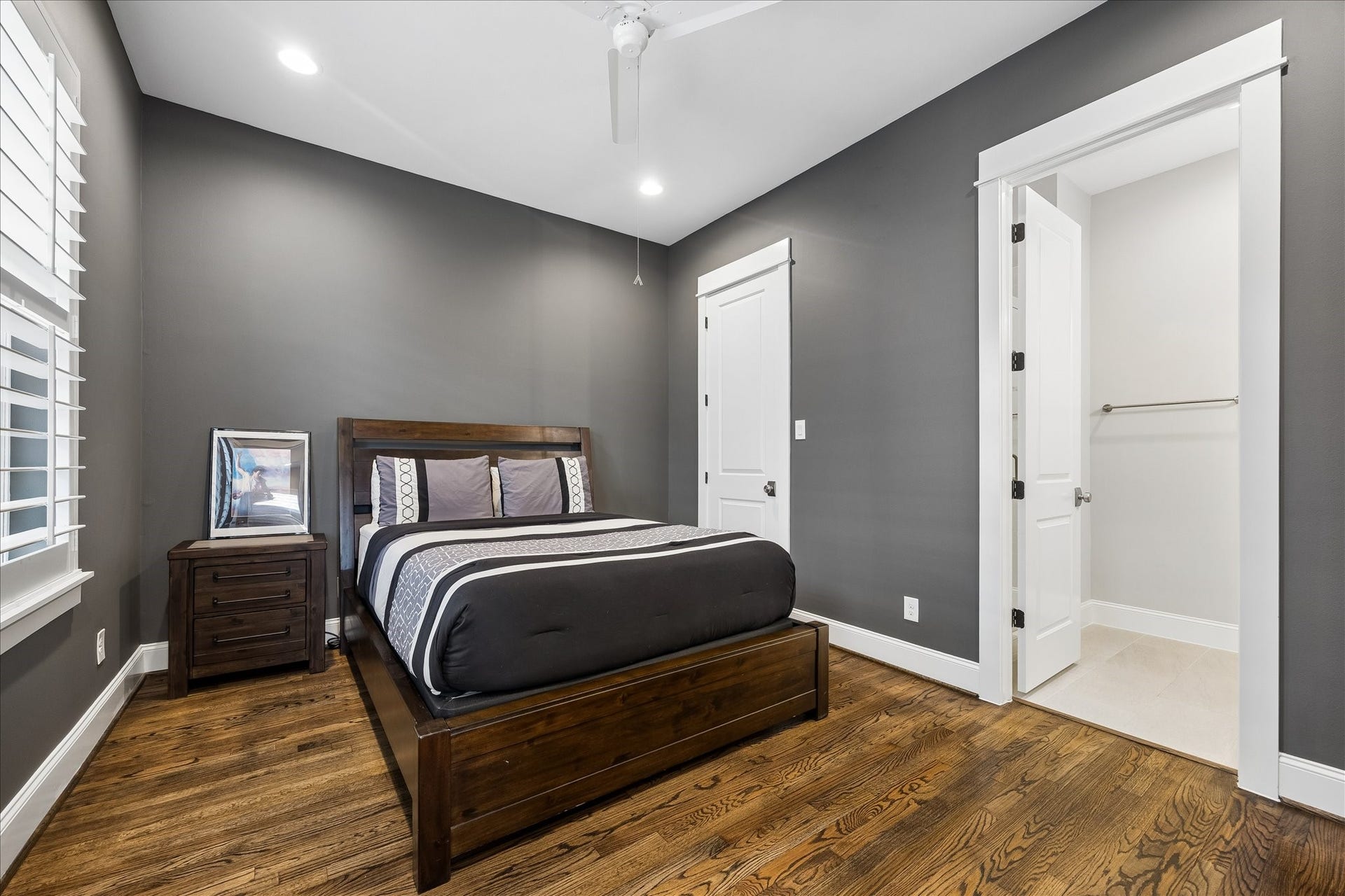2915 Hicks Street, Houston, TX 77007 Chic and modern secondary bedroom featuring hardwood floors, sleek gray walls, and ample natural light with a door that leads to an adjoining bathroom, offering convenience and privacy.