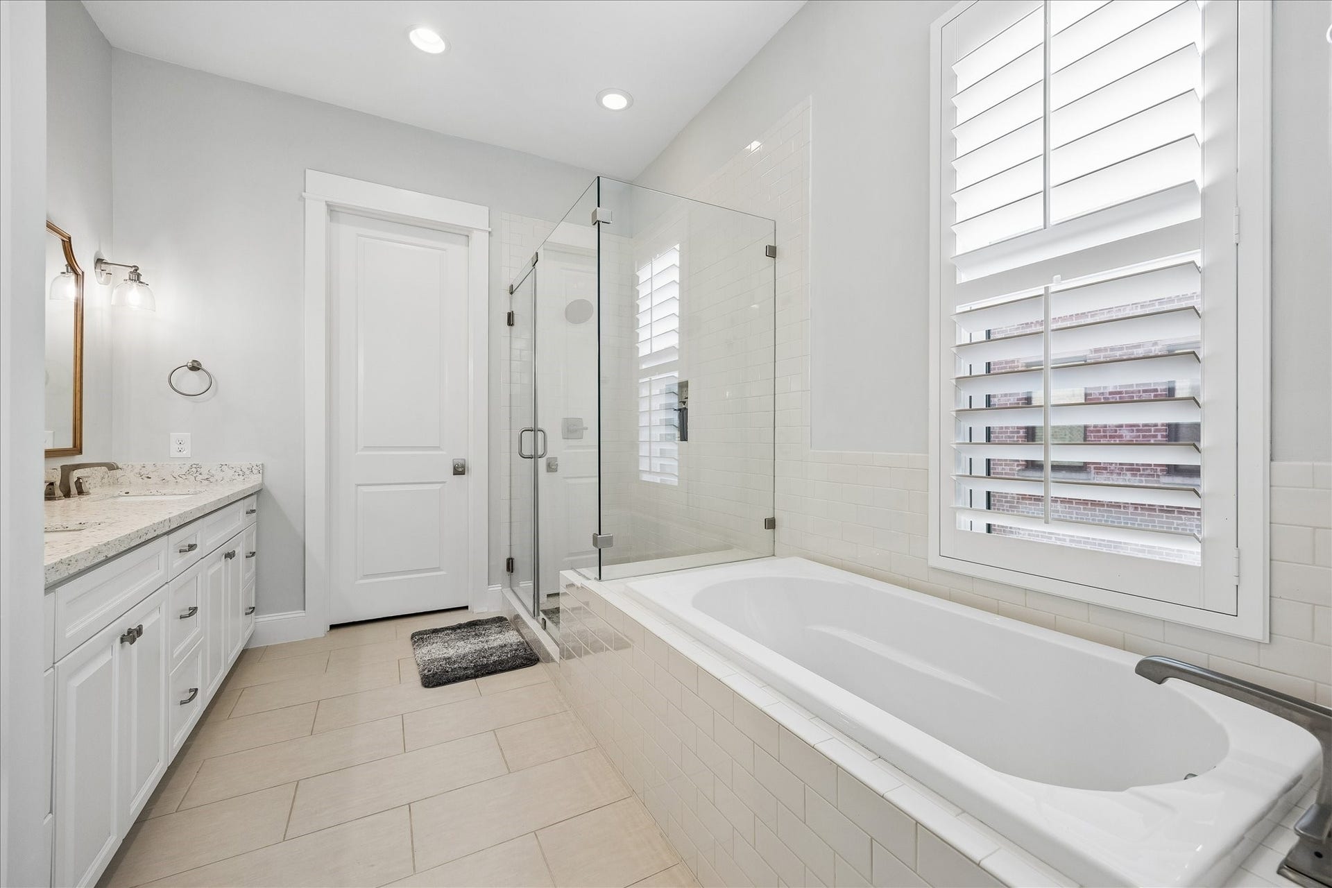 2915 Hicks Street, Houston, TX 77007 Elegant bathroom featuring a spacious walk-in shower, luxurious soaking tub, and double vanity with granite countertops. Natural light streams through plantation shutters, enhancing the bright and airy feel.