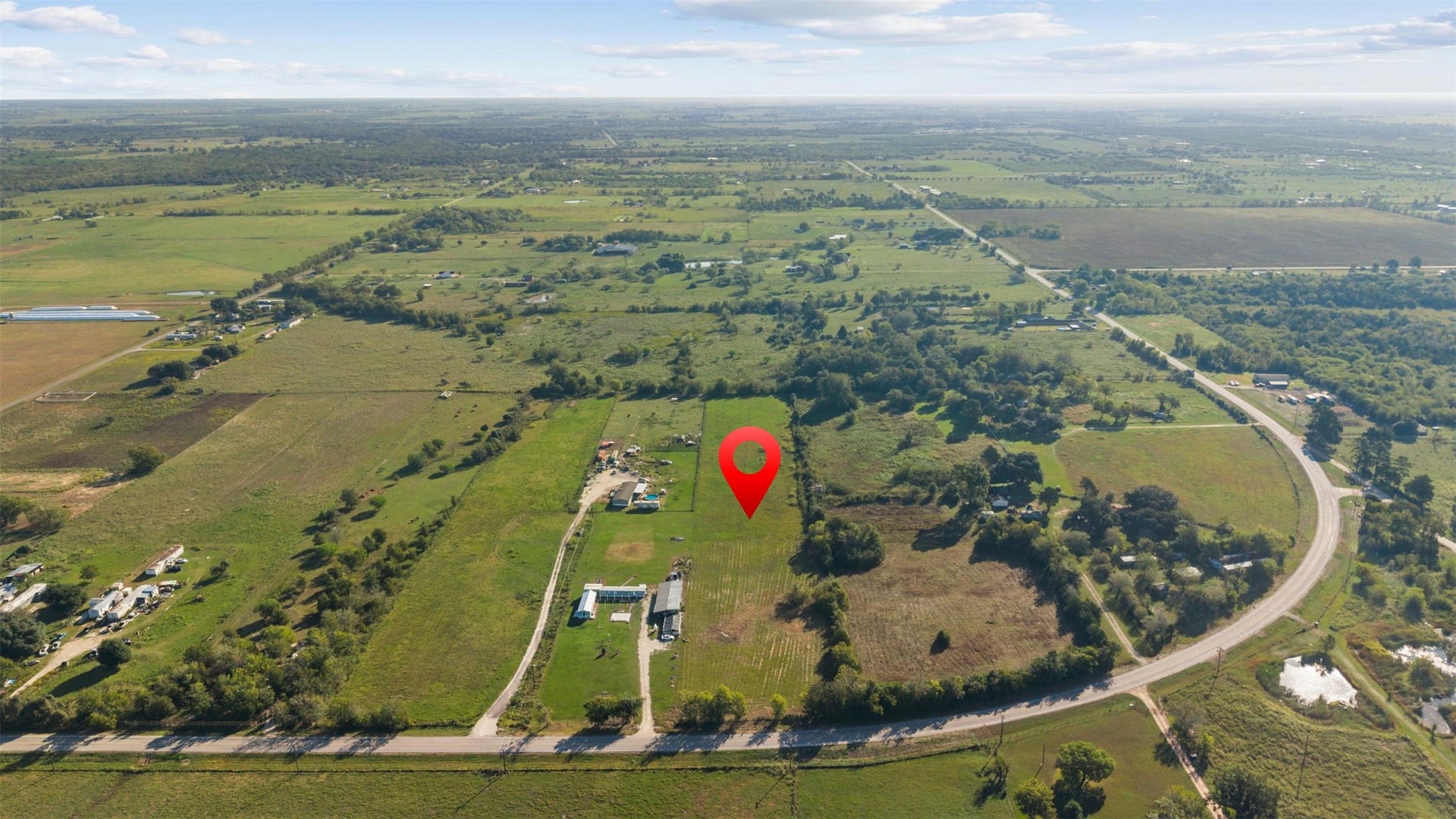 East-facing aerial capturing the property's position along the gentle curve of FM 1887, with open fields, scattered homesteads, and stretches of countryside extending toward the horizon.