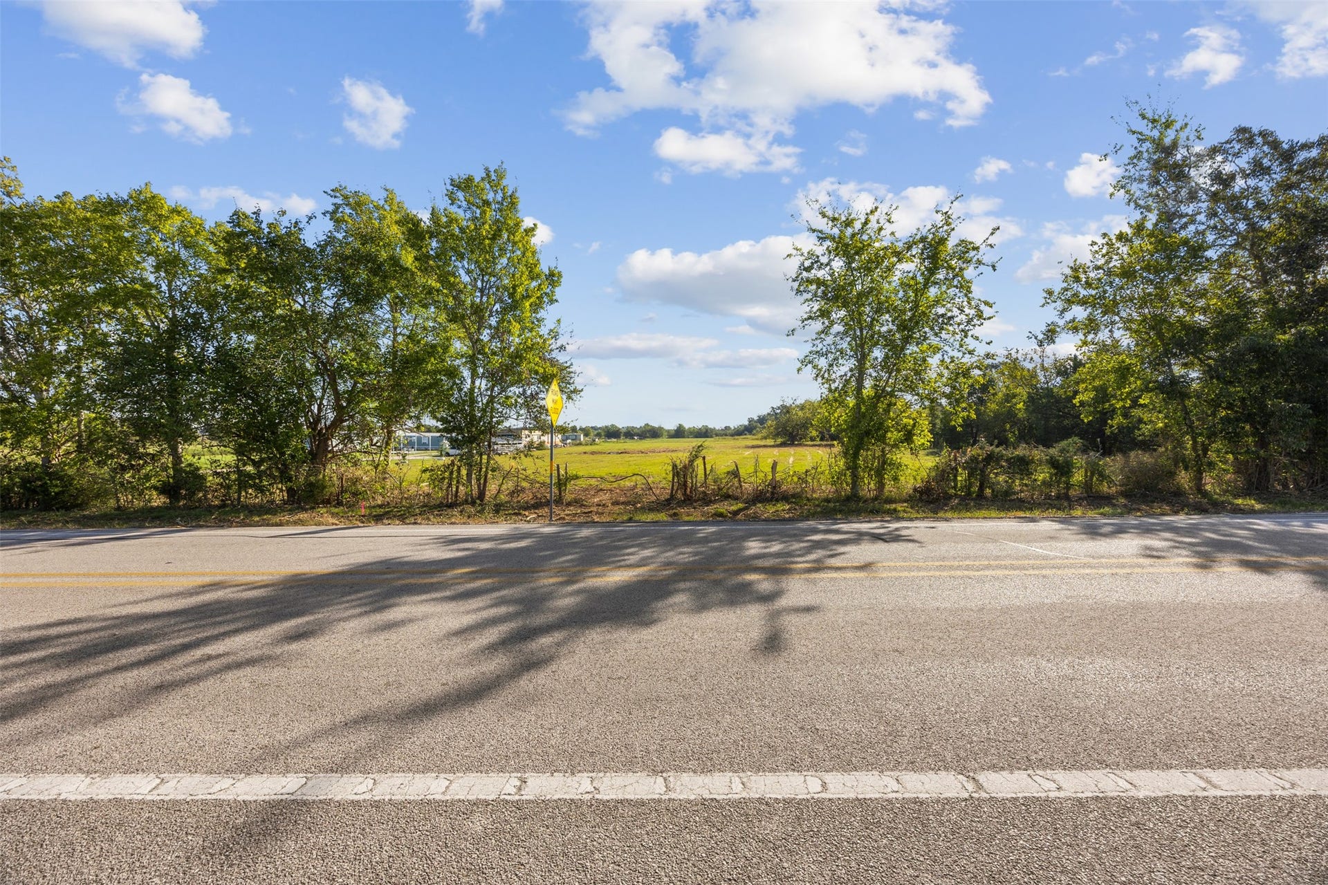 A view from FM 1887 looking east across the property, offering a glimpse of the cleared landscape nestled between established trees along the roadside.