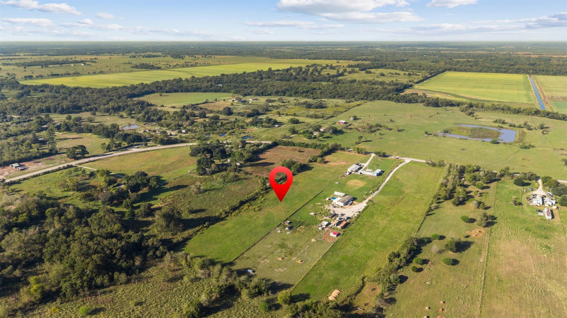 Southwest-facing aerial showcasing the property's location amid the rolling stretches of pastureland, wooded areas, and neighboring rural properties that define the Waller County countryside.