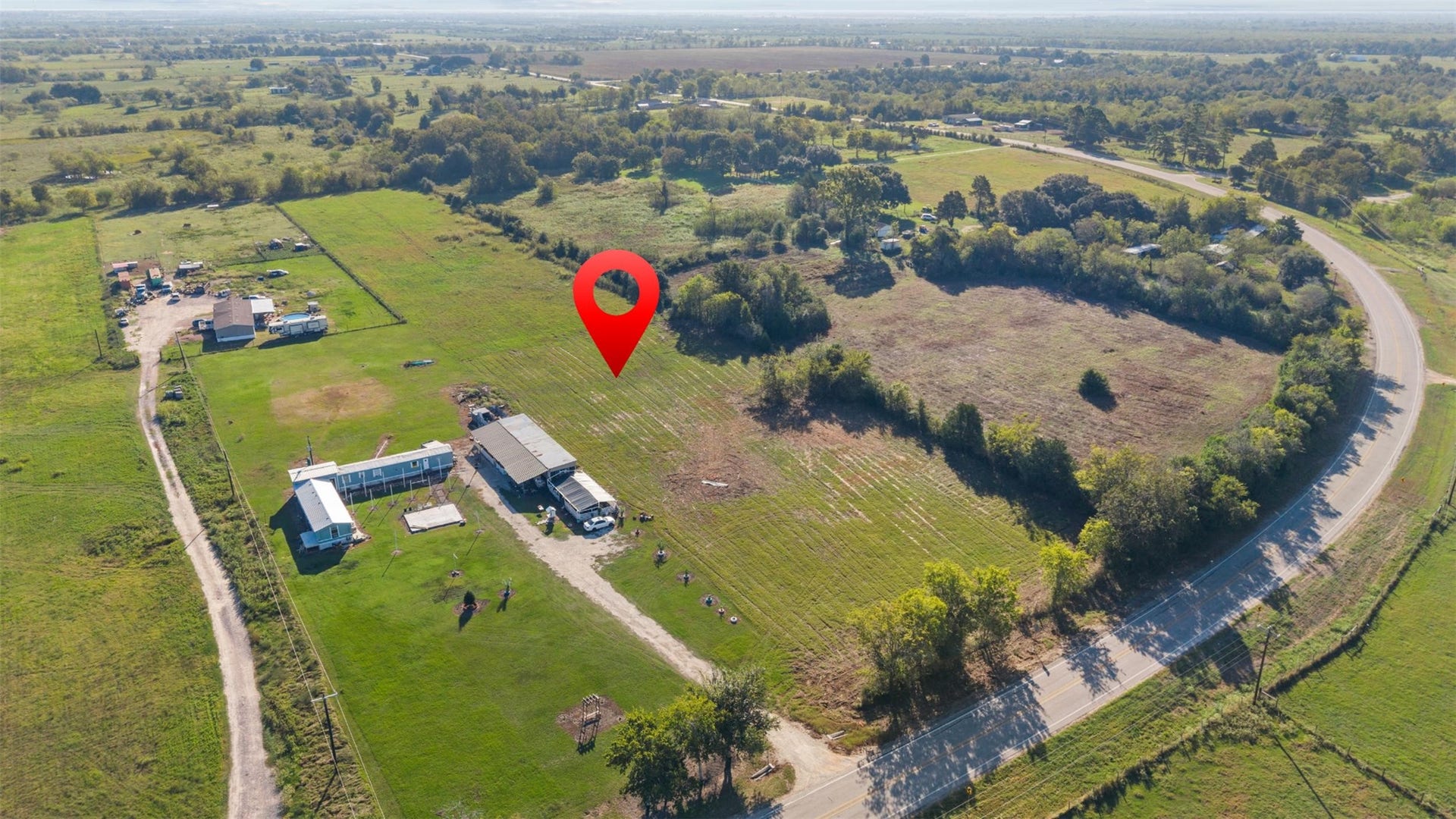 Southeast-facing aerial offering a closer look at the property's cleared acreage, natural tree coverage, and frontage along the curve of FM 1887.