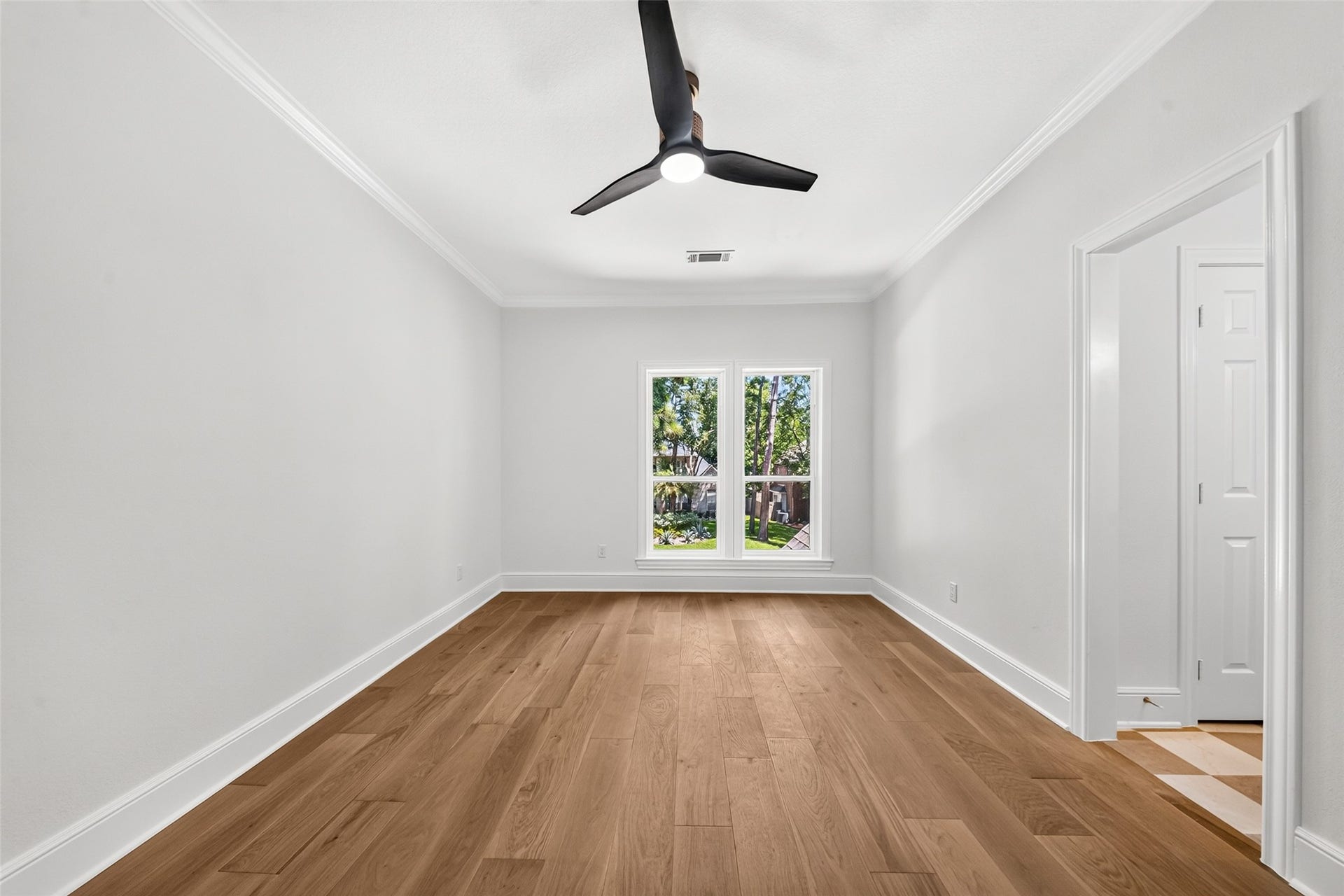 46 Pebble Cove Drive, The Woodlands, TX 77381 Bright and spacious room featuring elegant hardwood floors, a modern ceiling fan, and large windows inviting abundant natural light.