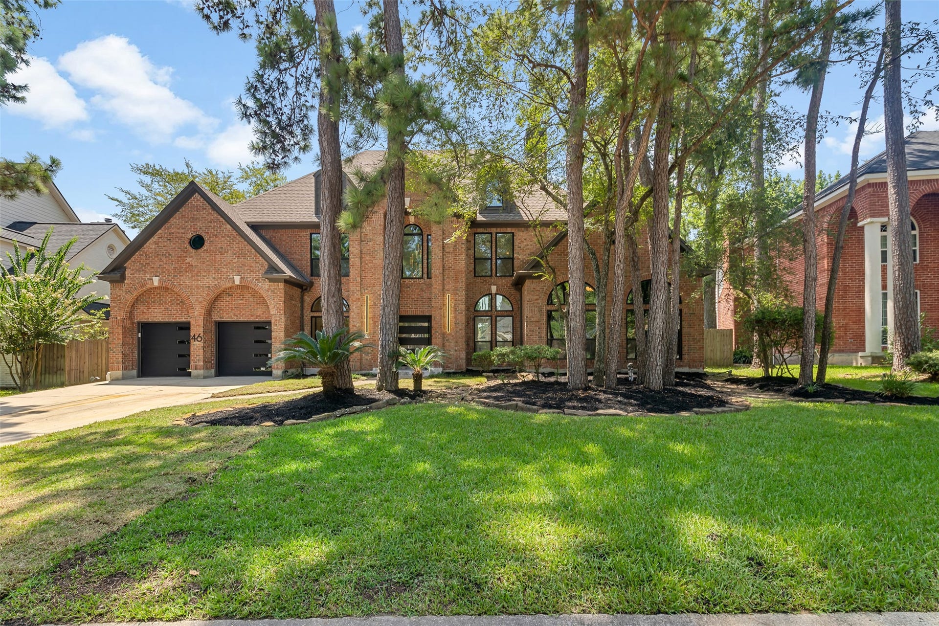 46 Pebble Cove Drive, The Woodlands, TX 77381 Stately brick home nestled among mature trees, featuring a charming arched double garage and expansive windows for abundant natural light.
